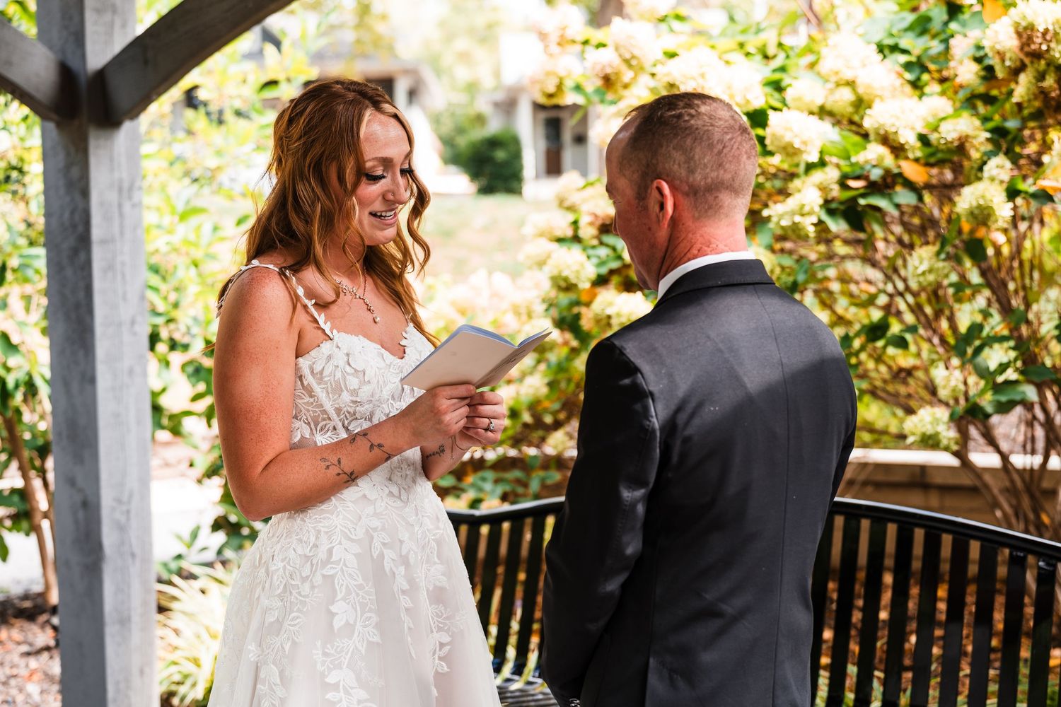 Wedding ceremony taking place in a garden setting with white chairs and floral decorations.