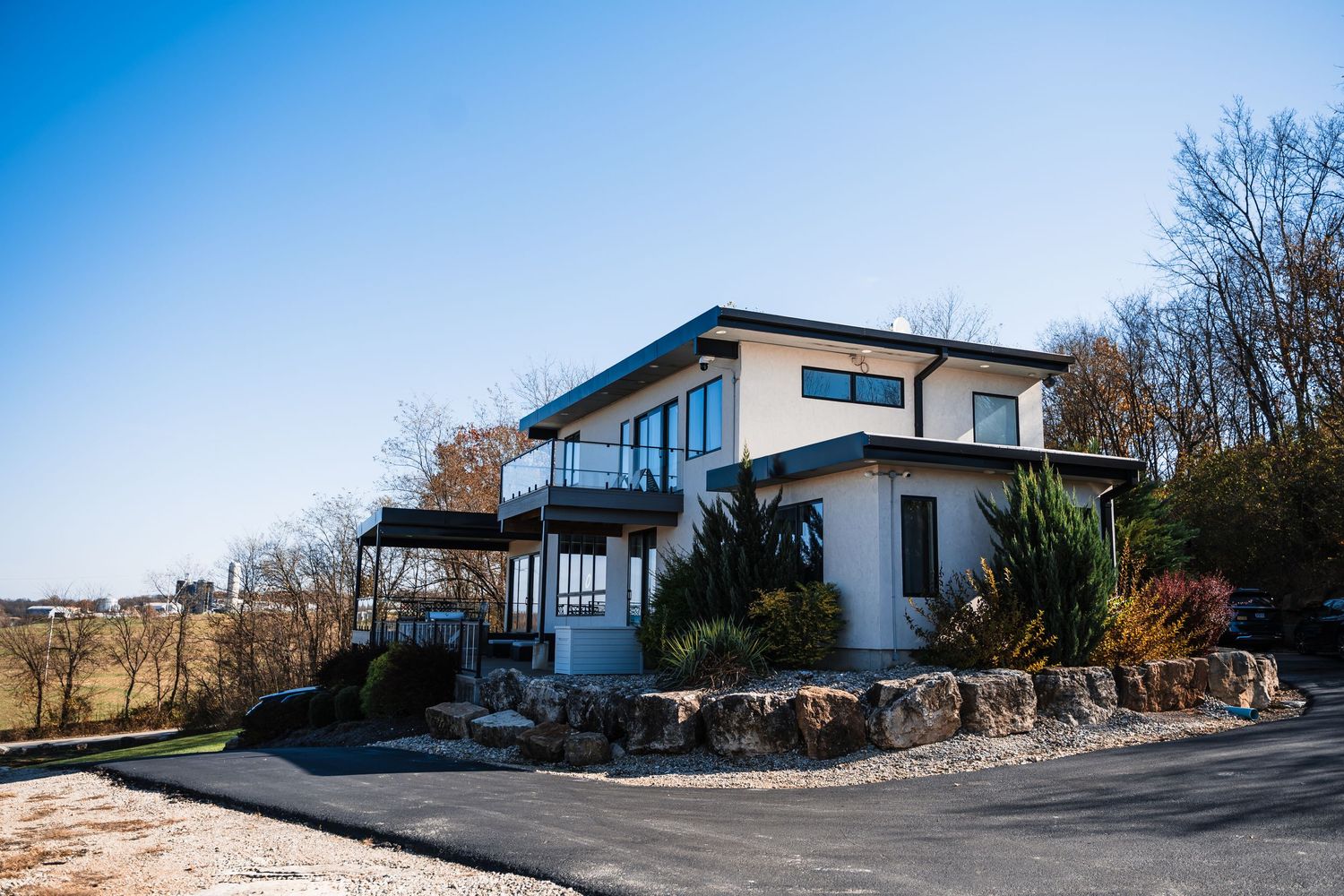 Modern two-story white house with stone retaining wall and large windows overlooking scenic landscape.