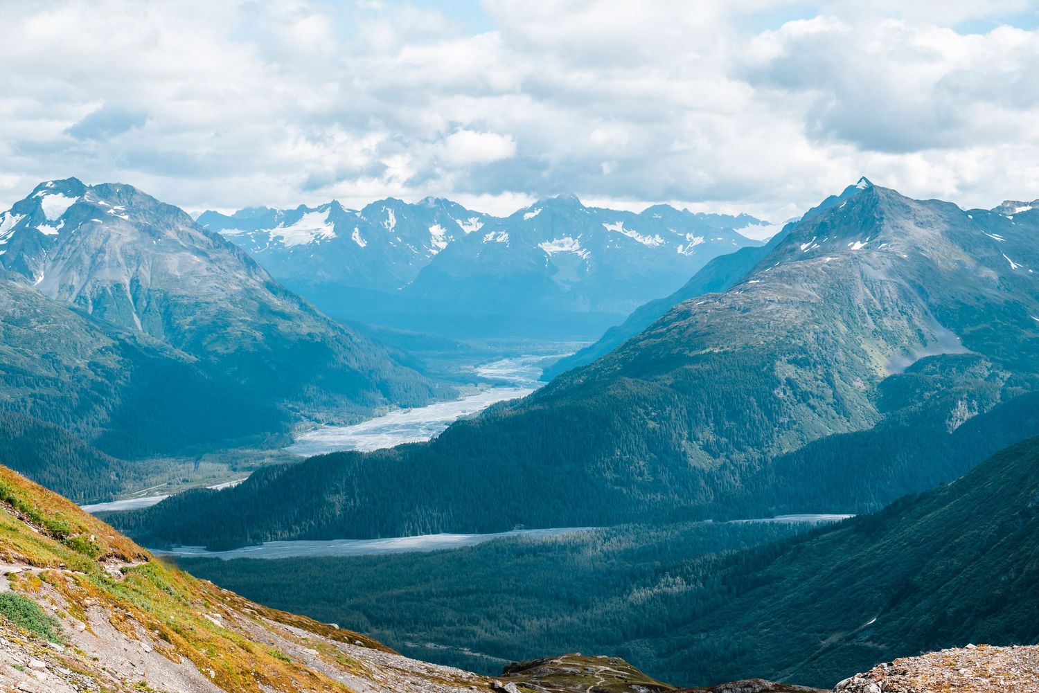A scenic mountain landscape with snow-capped peaks and blue lakes nestled between valleys in a rugged terrain.