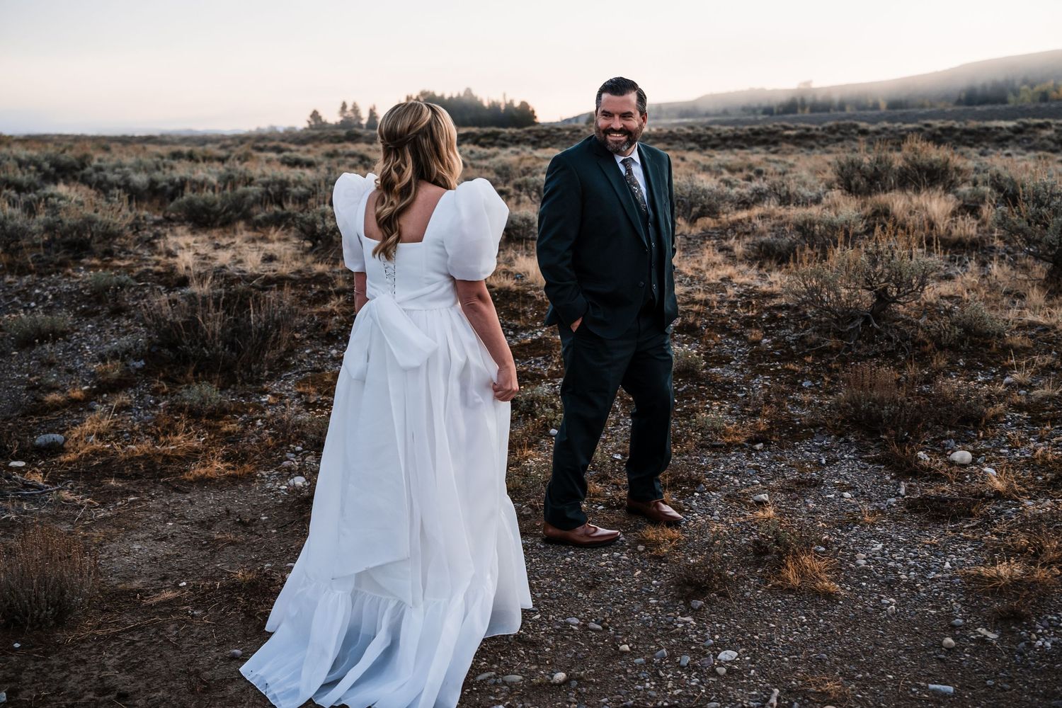 A couple shares an intimate moment in their wedding attire against a rugged outdoor landscape at sunset.