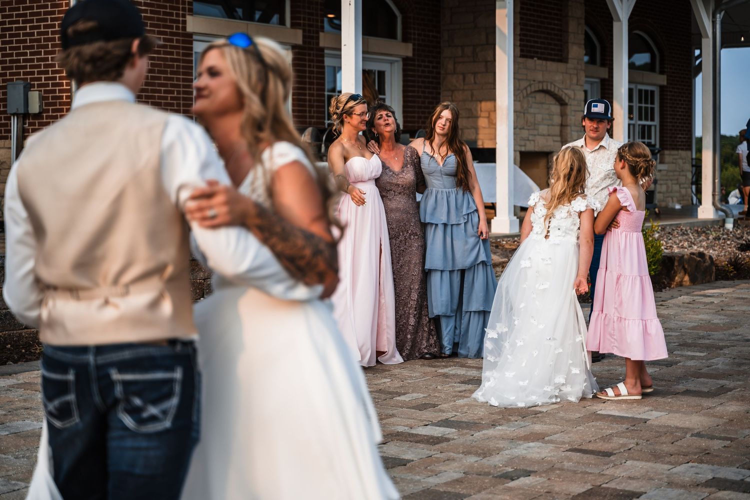 Wedding celebration on a beautiful stone patio with bridesmaids in pink and blue dresses watching the first dance.