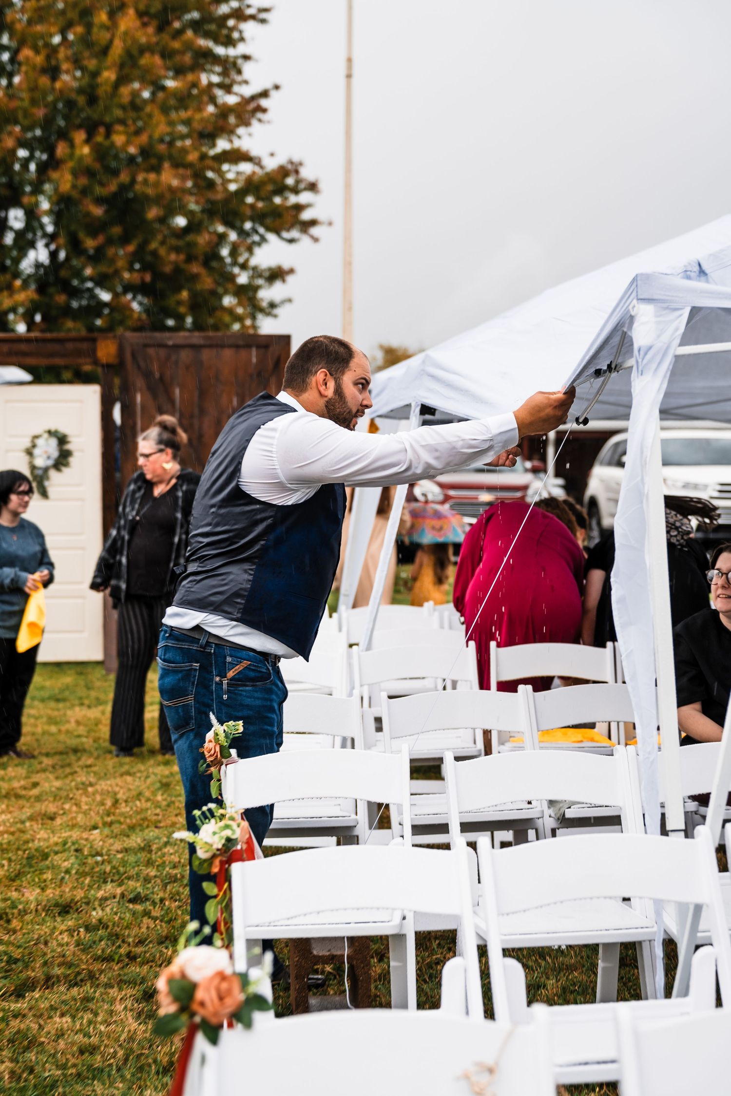 White chairs being set up outdoors for a wedding ceremony on a grassy lawn.