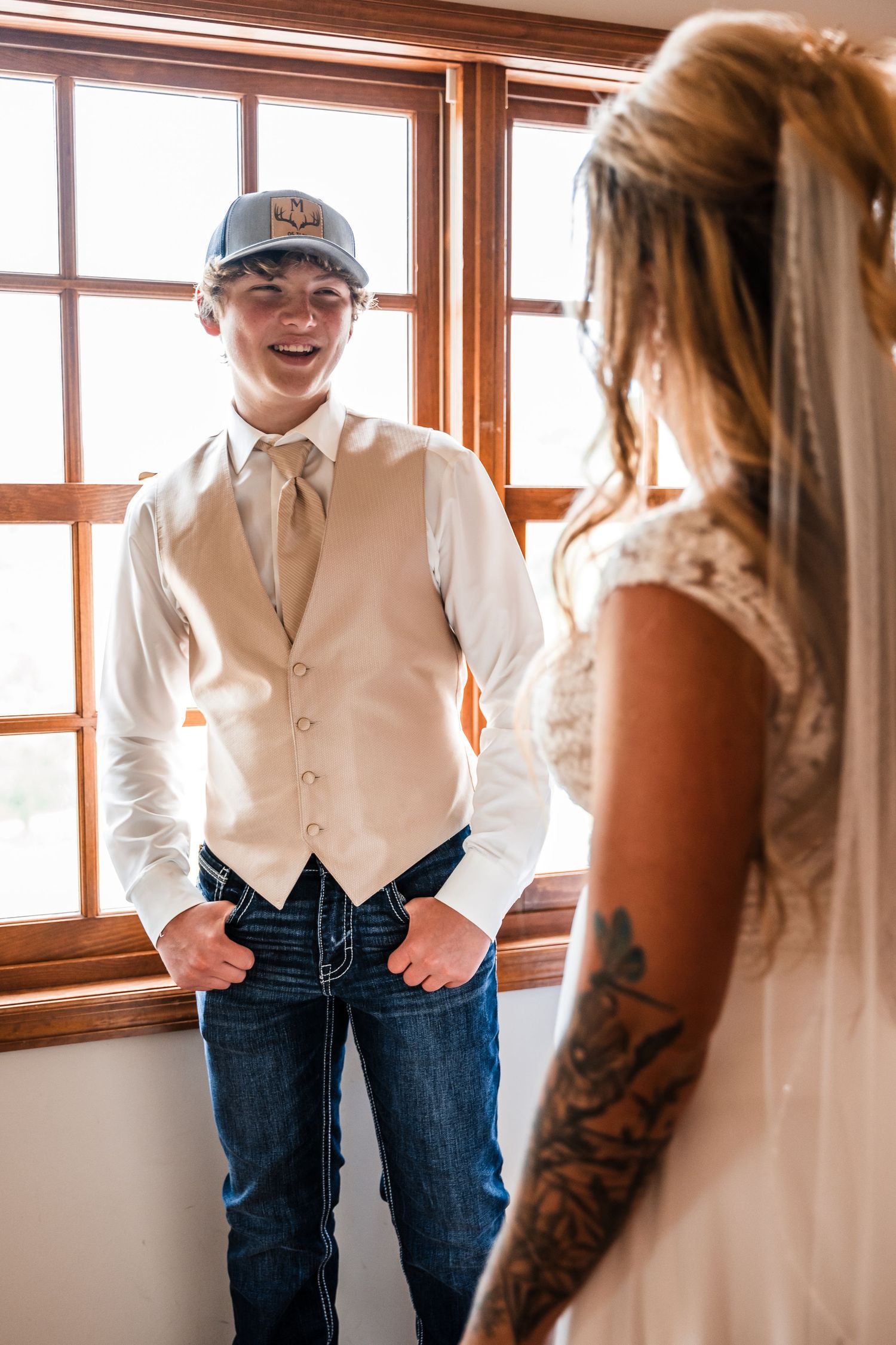 Casual wedding attire with vest, jeans and baseball cap during preparation moment.