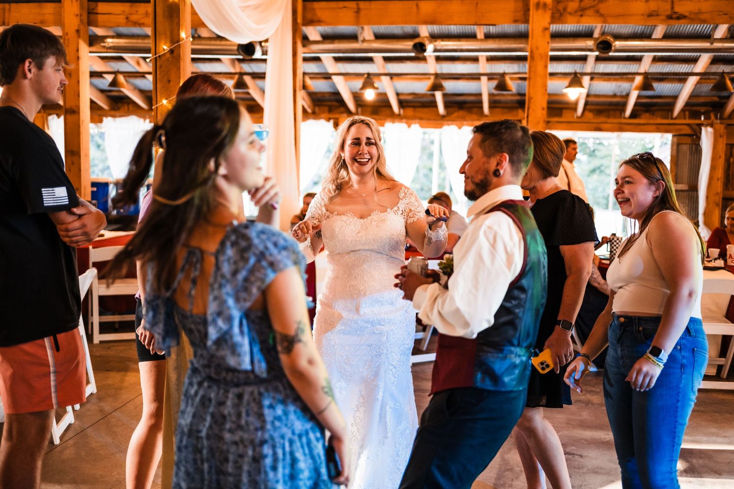 Wedding celebration in a rustic indoor venue with guests gathered around a dancing couple.