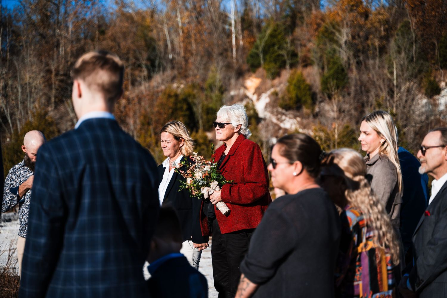 Outdoor gathering of formally dressed people by waterfront during autumn season.