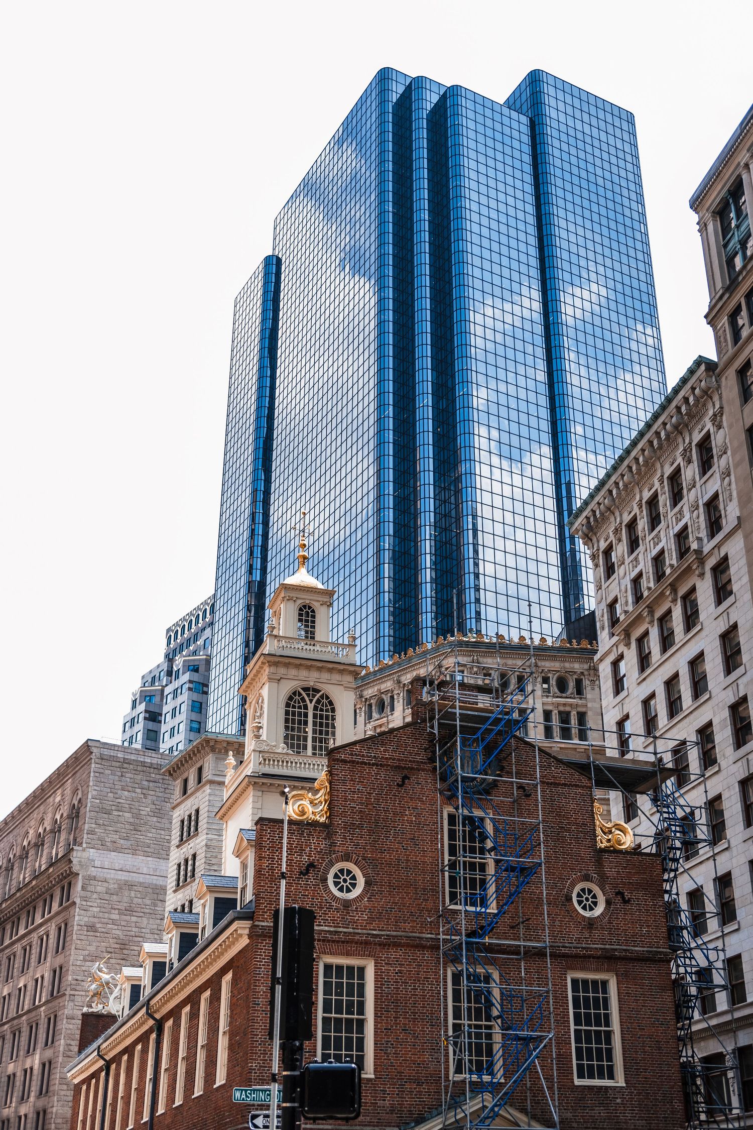 Modern glass skyscraper towers over historic Old State House building in downtown Boston.