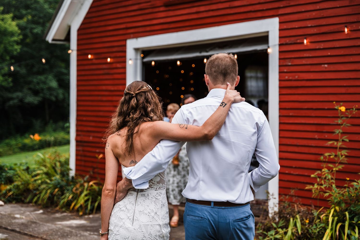 Newlyweds embrace while walking towards a red barn on their wedding day.