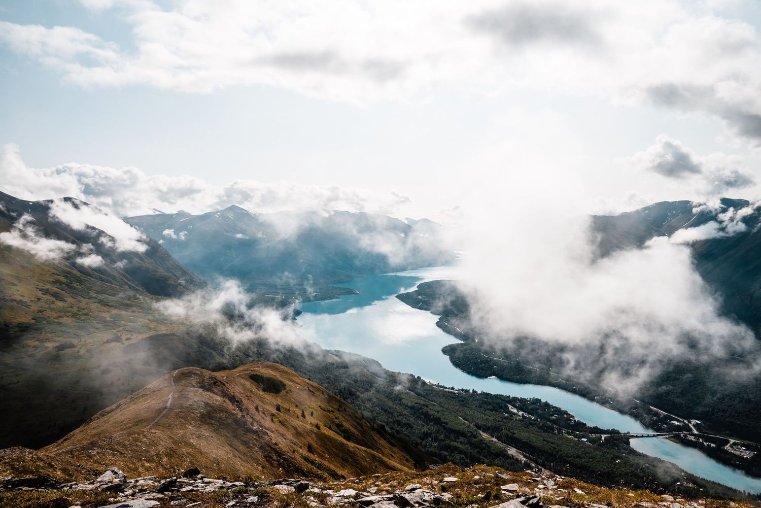 Misty mountain vista overlooking a turquoise alpine lake winding through valleys.