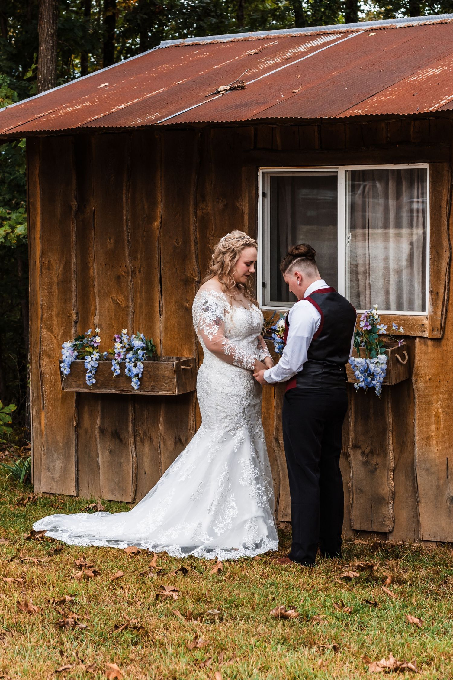 A rustic cabin with a metal roof and flower boxes serves as a backdrop for a wedding ceremony.
