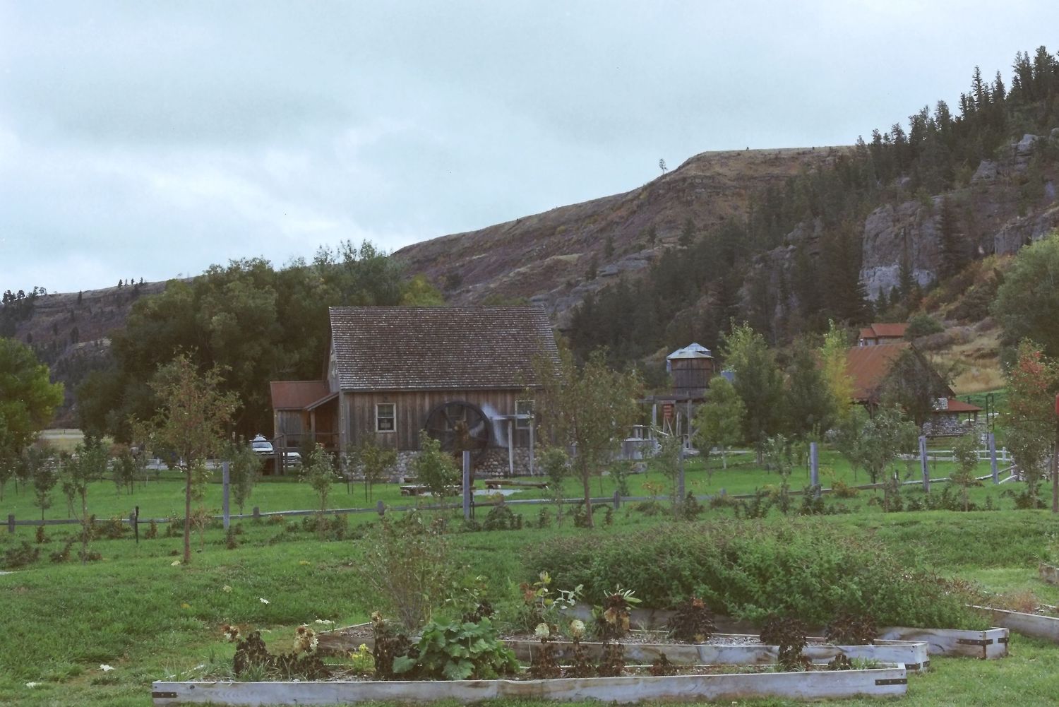 Panoramic mountain landscape with rustic wooden buildings nestled among green hills and a winding stream.