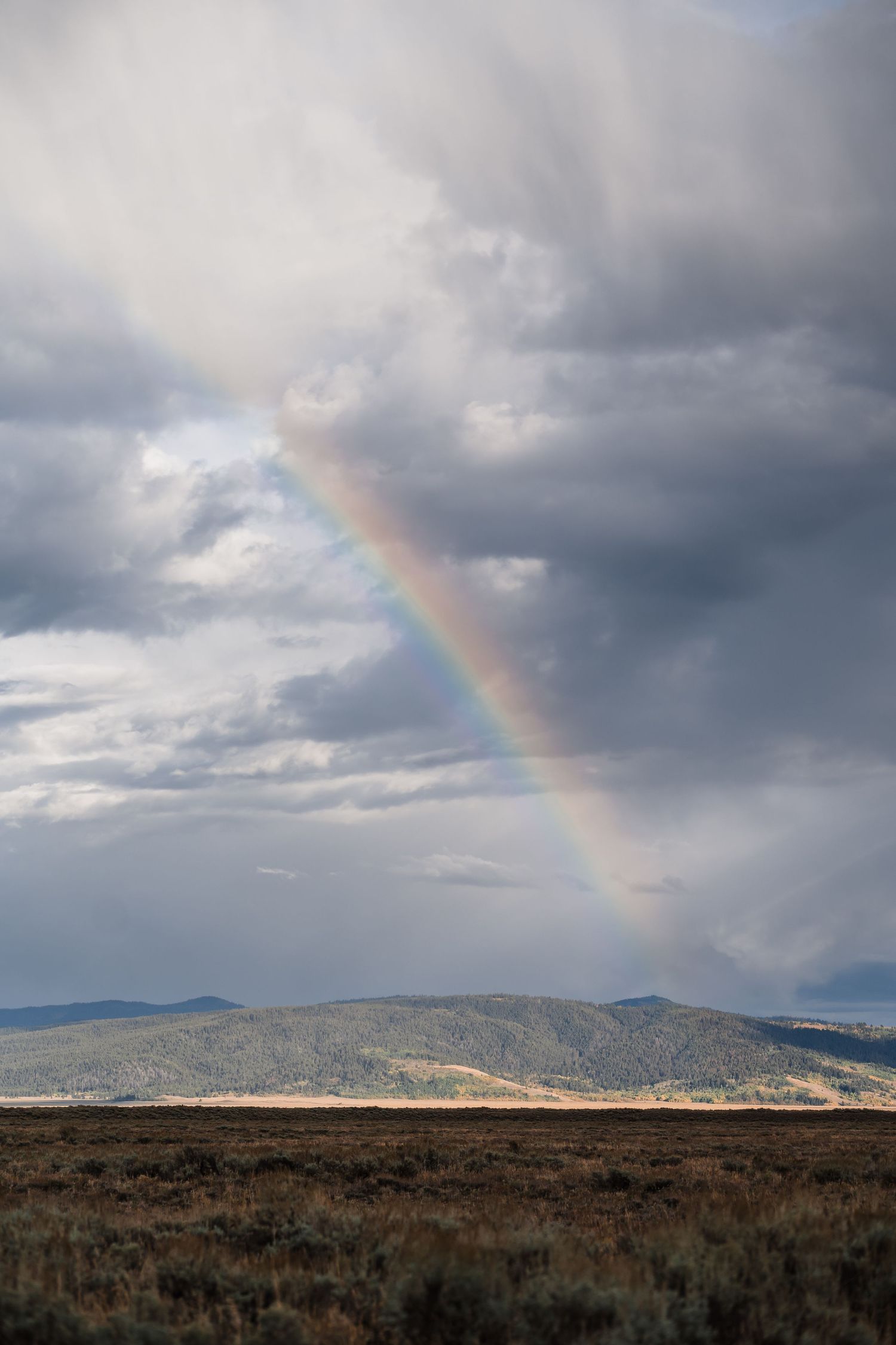 Vibrant rainbow arches over rugged mountain landscape with stormy clouds.