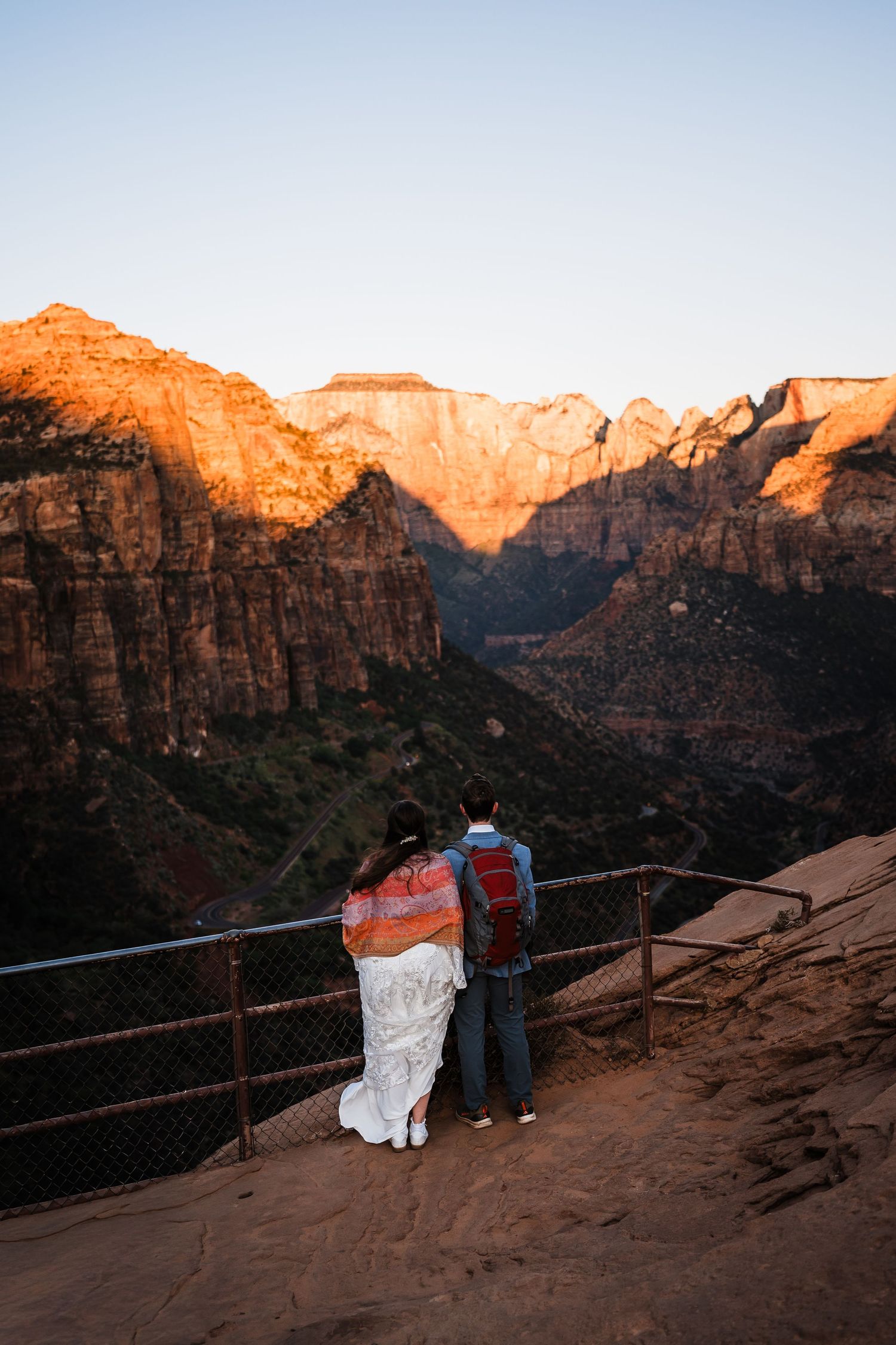Couple embracing at overlook viewing stunning Zion National Park canyon at golden hour sunset.
