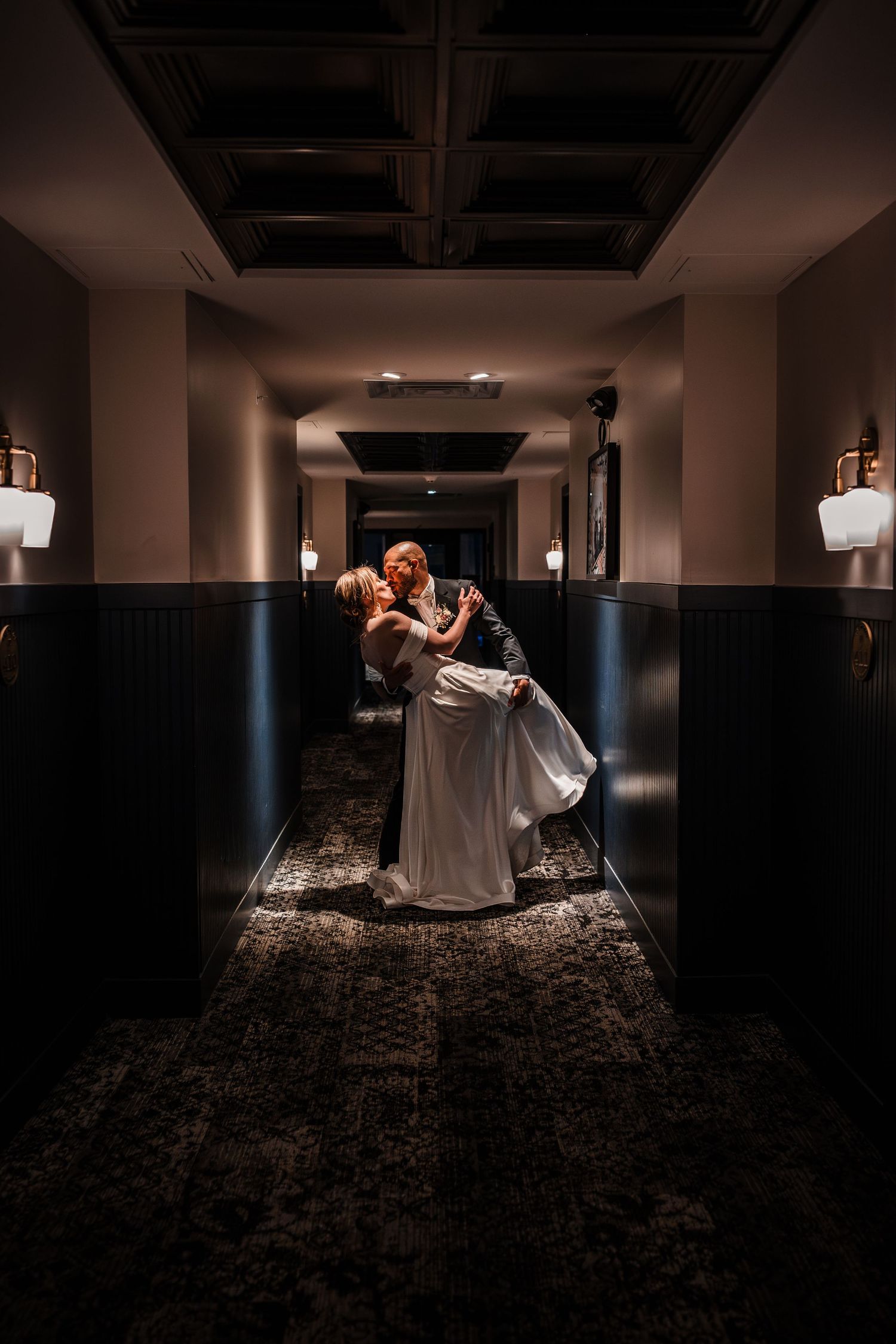 Groom dipping bride in dimly lit elegant hotel hallway for a dramatic romantic wedding portrait.