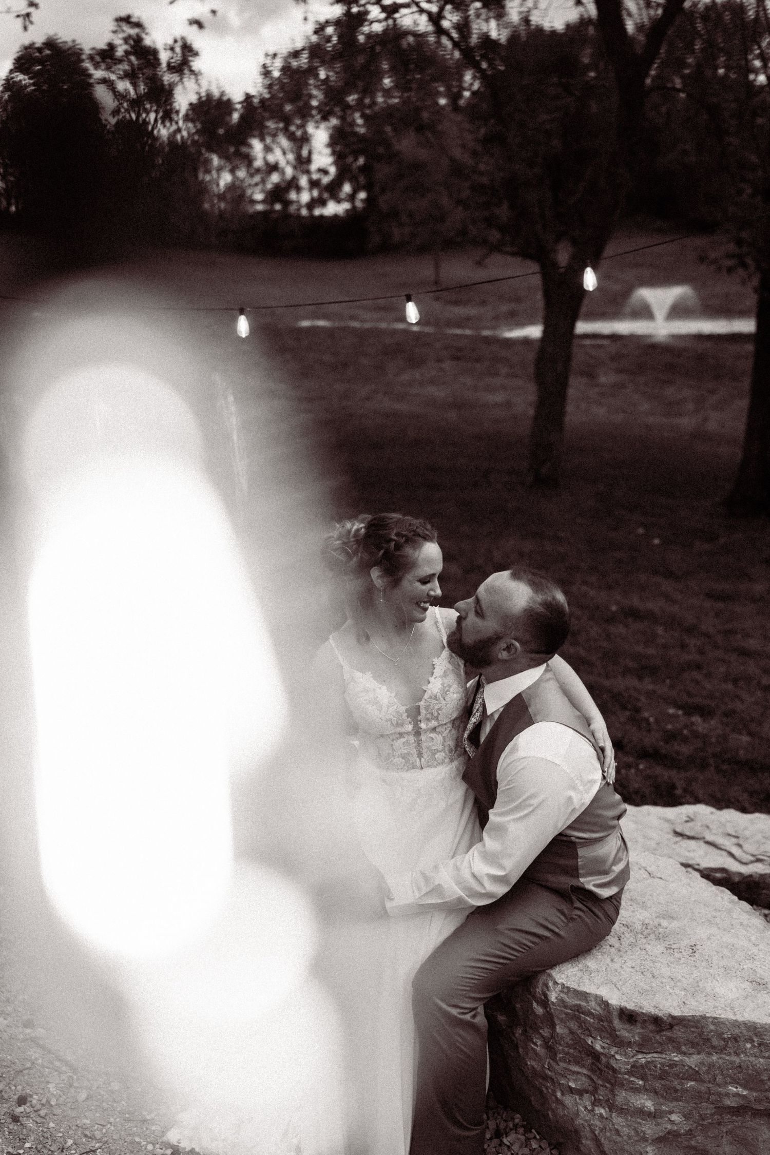Black and white romantic photo of bride and groom sitting on rocks at dusk.