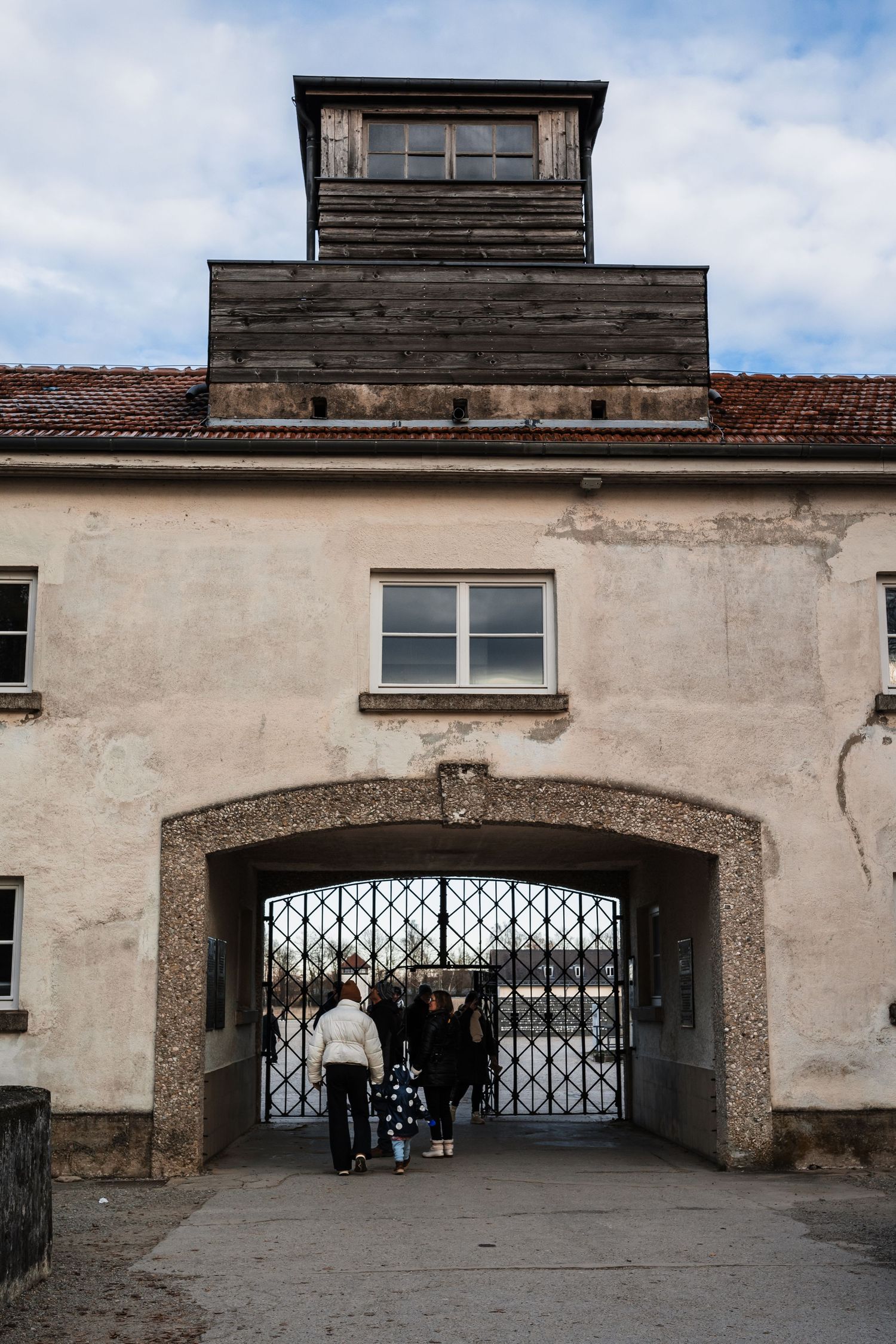Entrance gate to Dachau concentration camp with guard tower and iron gates under cloudy sky.