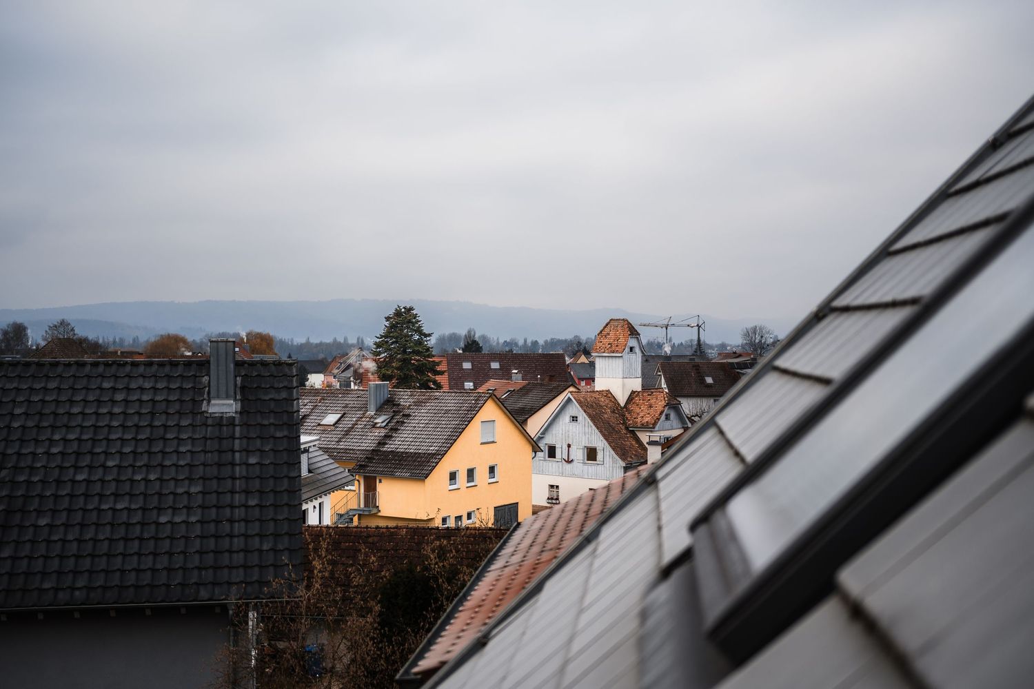 A row of residential rooftops with dormers and windows against a cloudy sky in a suburban neighborhood.