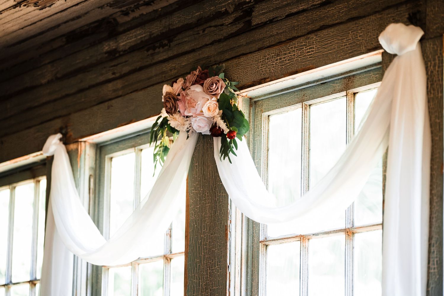 White fabric draped elegantly across rustic wooden beams for wedding ceremony backdrop.