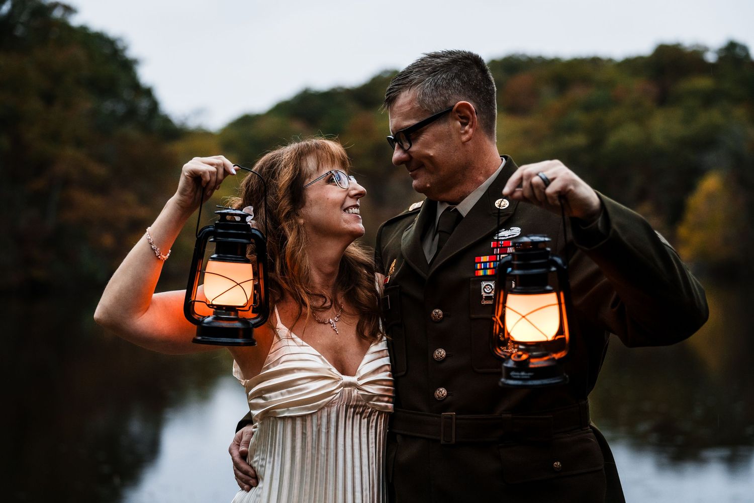 Couple holding lanterns during outdoor autumn photoshoot near lake.
