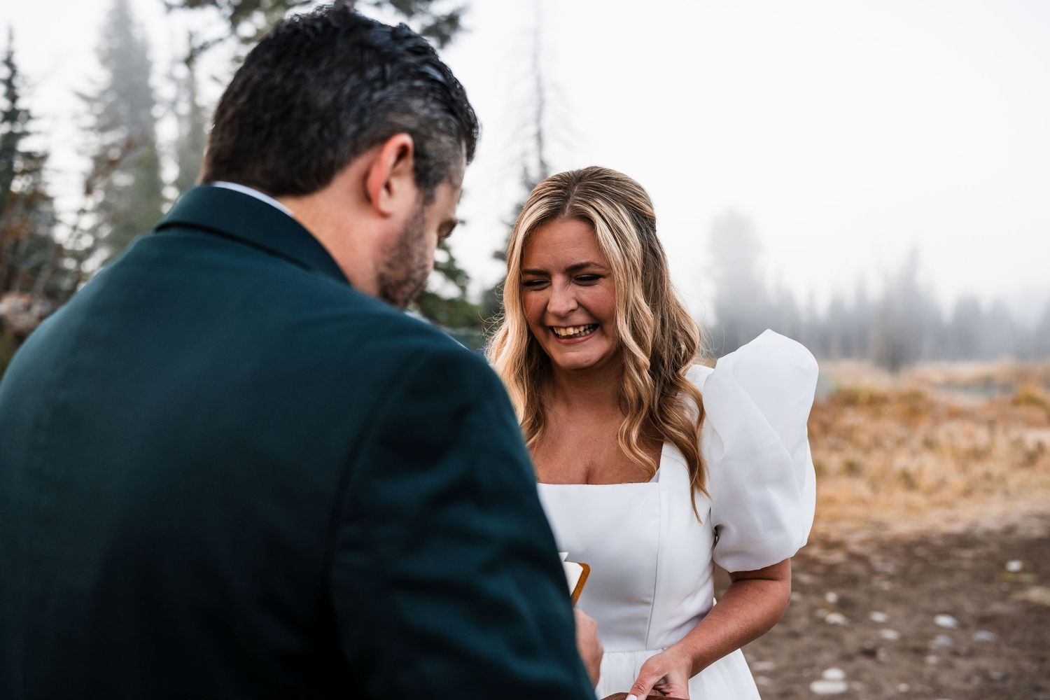 A joyful wedding moment captured in a misty outdoor forest setting at sunset.