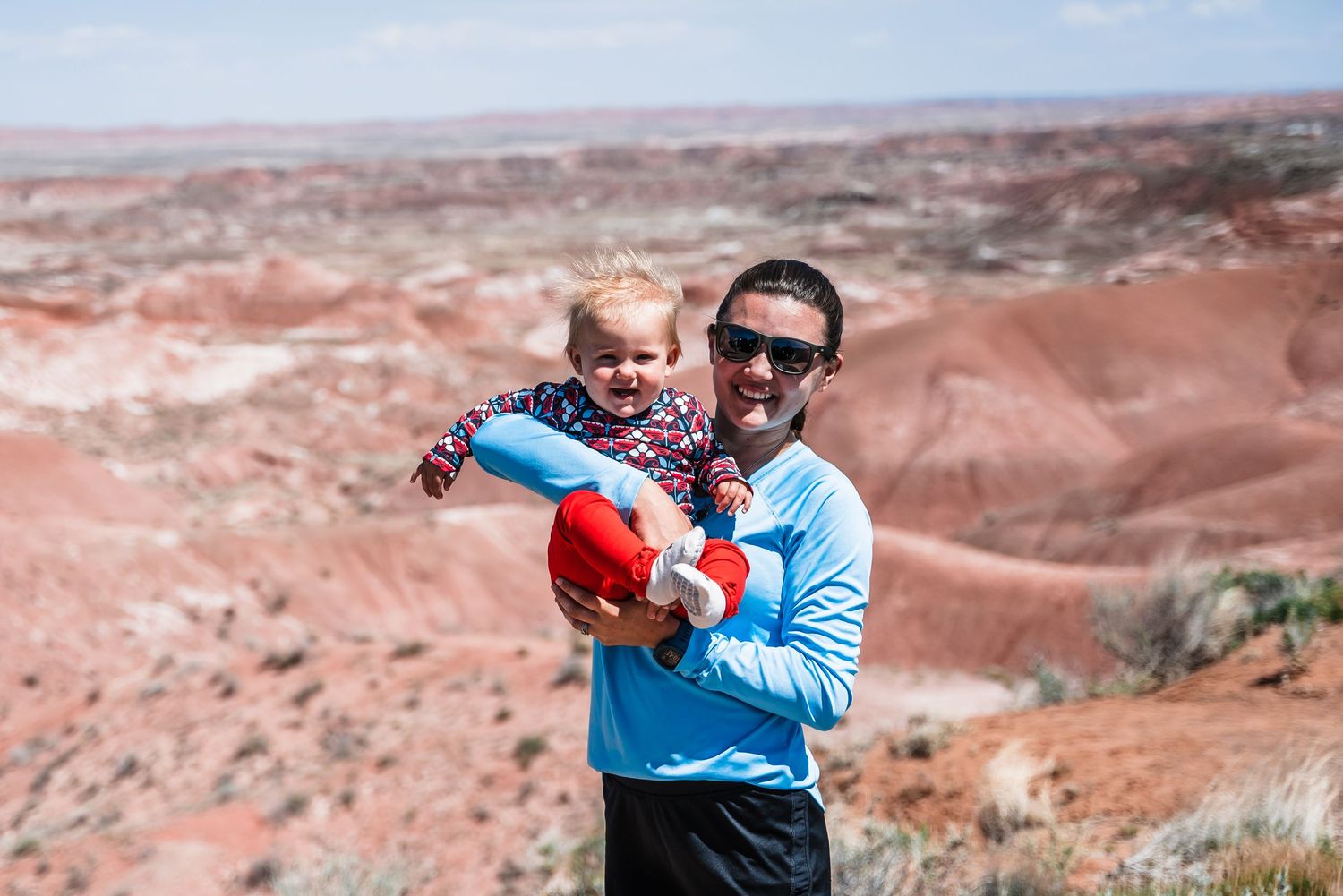 Parent and child enjoy sunny day against backdrop of red rock desert landscape in Painted Desert, Arizona.