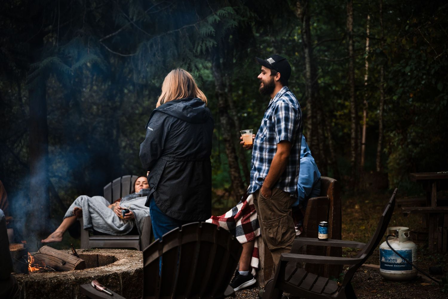 Evening gathering around a campfire with smoke drifting through the forest.