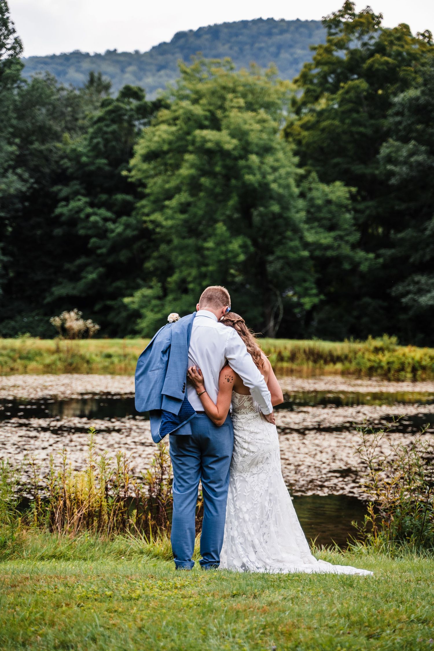 A romantic wedding moment captured from behind with mountain scenery and a pond in the background.