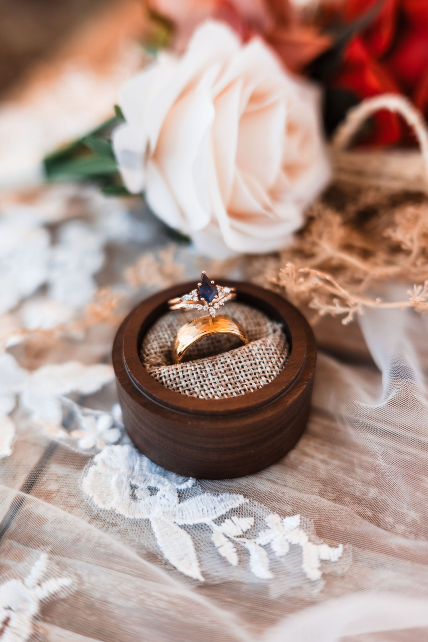 Wedding rings displayed in rustic wooden boxes with delicate lace and pink rose petals create an elegant composition.