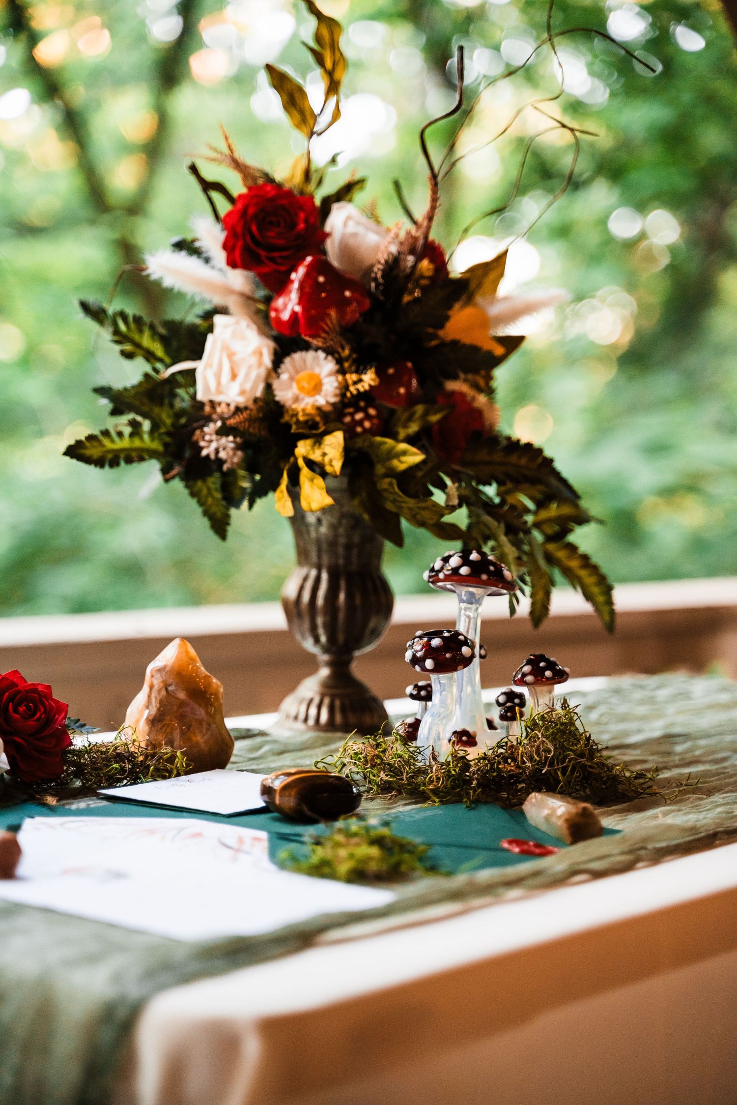 Whimsical woodland wedding decor featuring floral arrangements with red and pink blooms alongside decorative mushrooms.