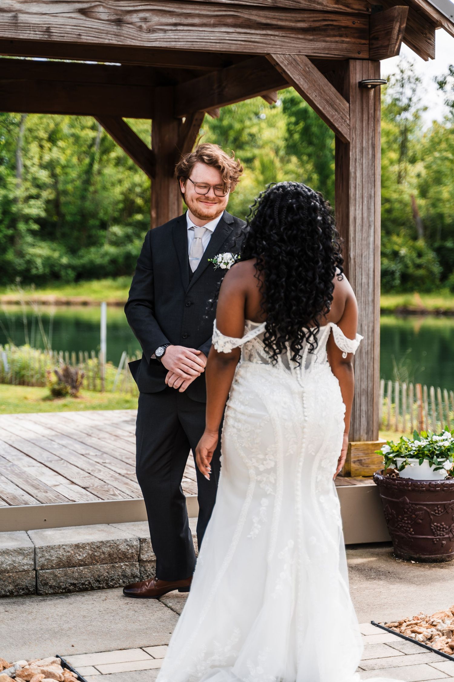 Groom smiling at bride in white mermaid wedding dress during first look at outdoor gazebo.
