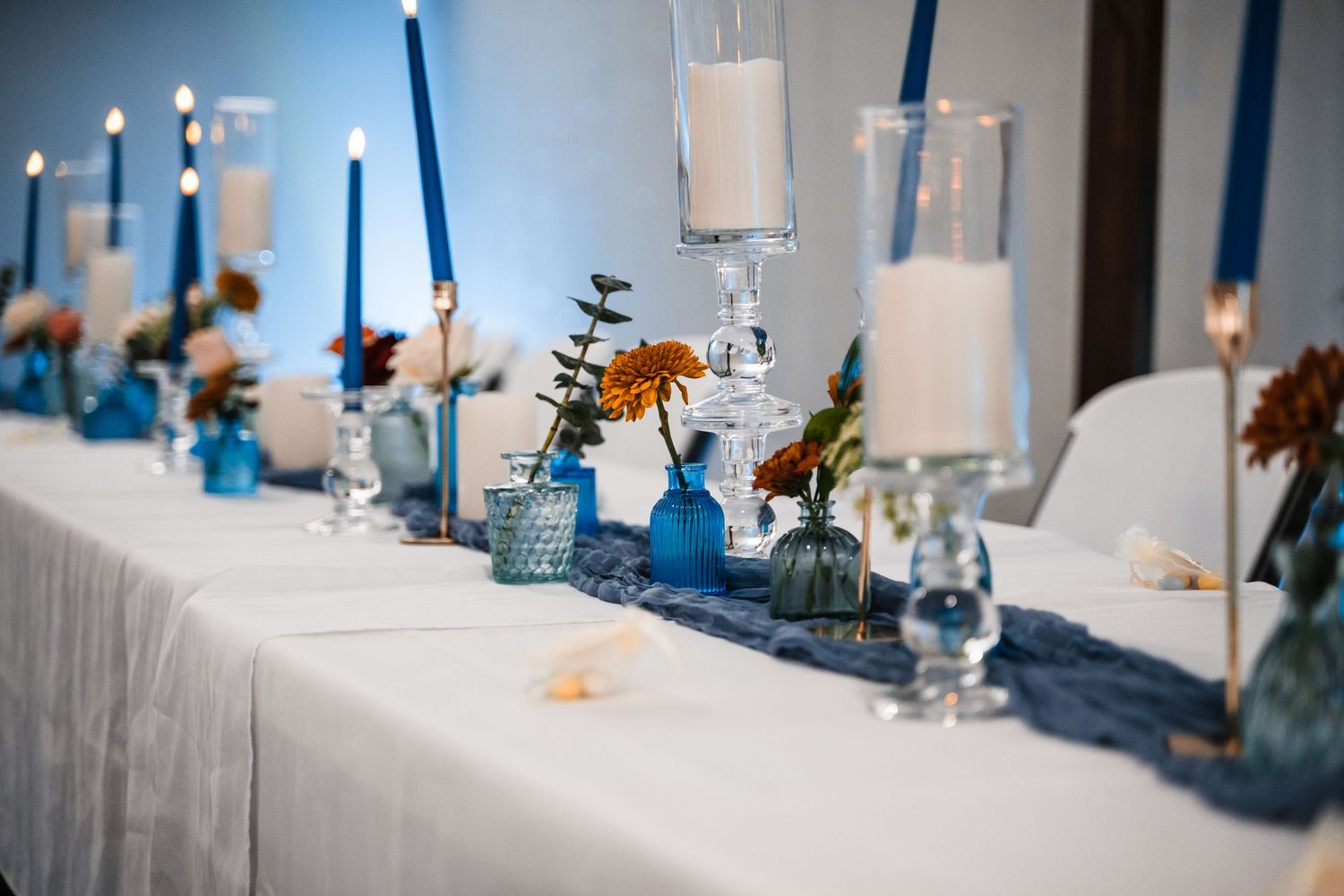 Wedding reception table decorated with blue candles and floral centerpieces.
