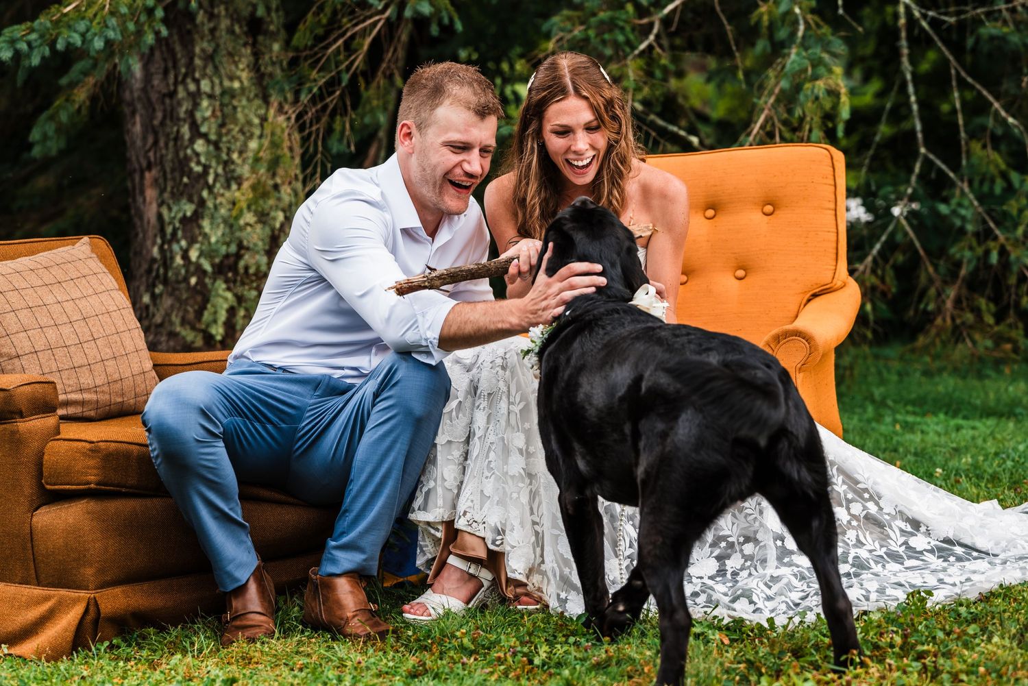 Couple sharing a moment with their black dog on orange vintage furniture outdoors.