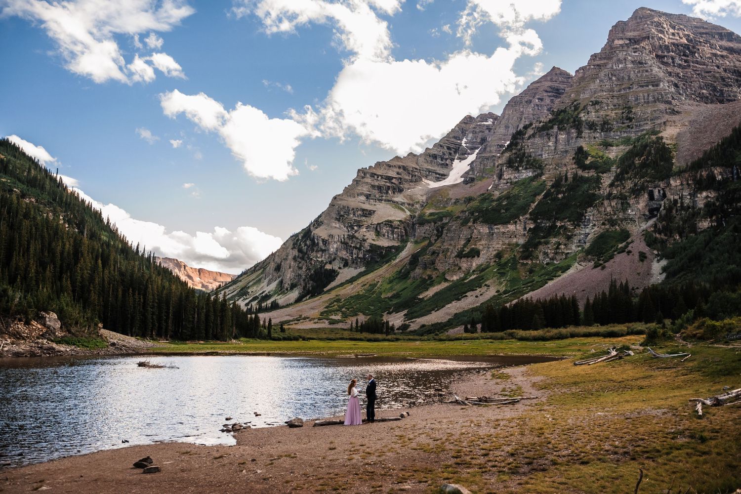 Scenic mountain lake landscape with dramatic peaks and two small figures on the shore.