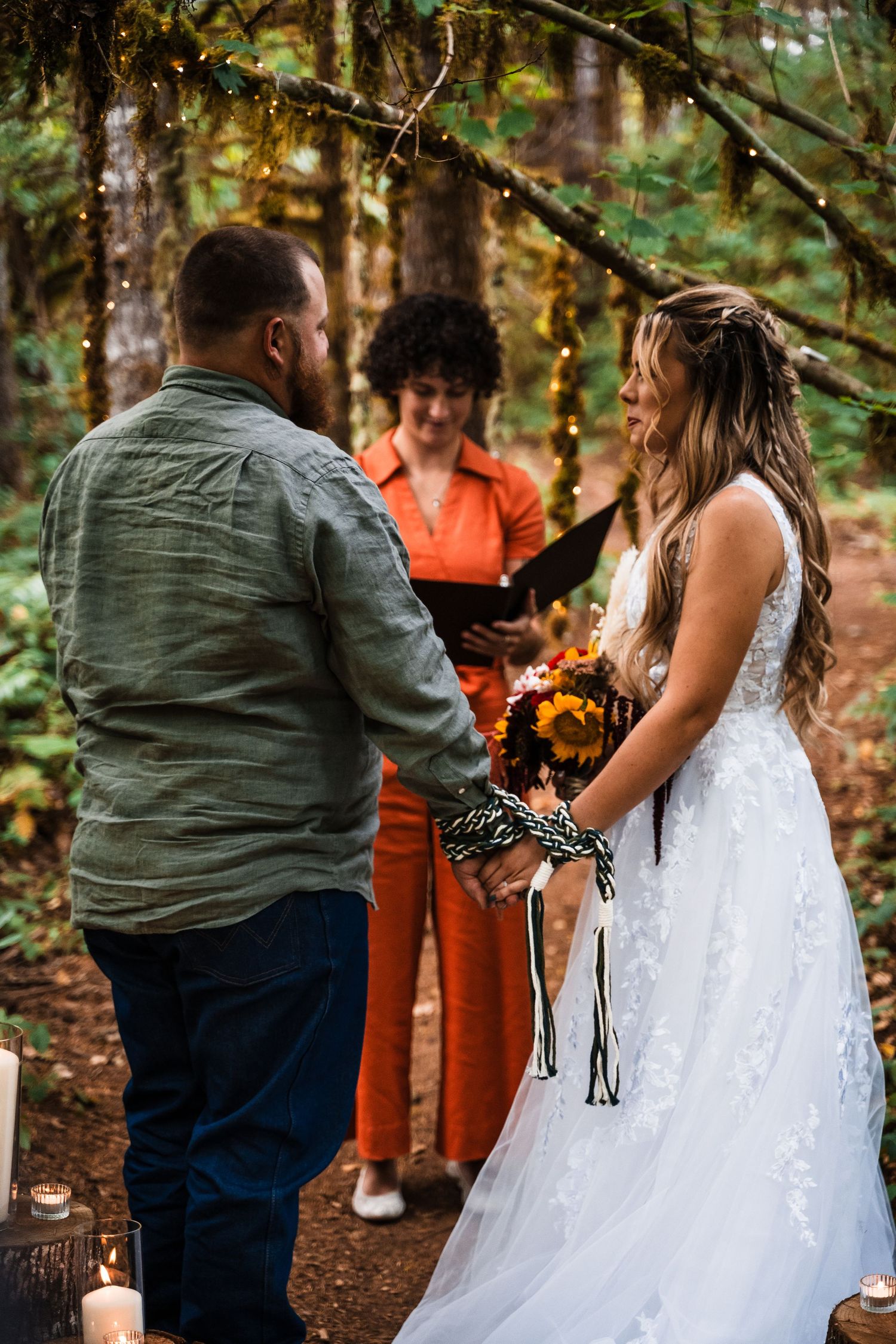 Wedding ceremony in progress on forest trail with fall-themed bouquet and candle decorations.
