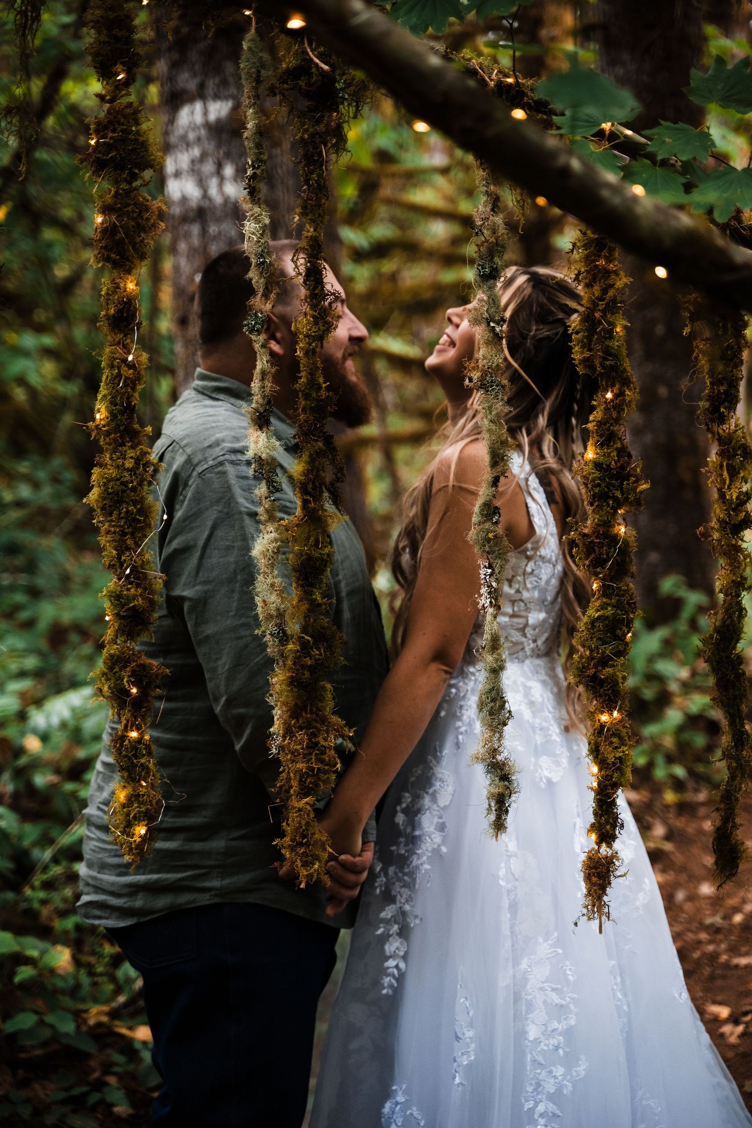 Couple holding hands in a mossy forest with sunlight filtering through trees.