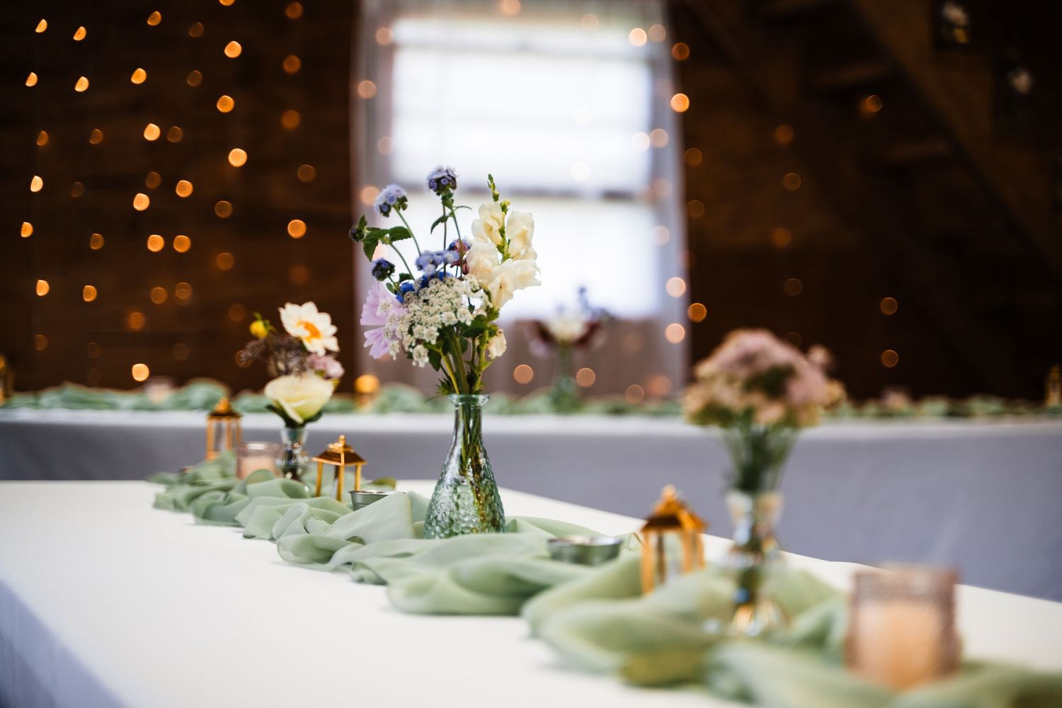 Wedding reception table settings with delicate floral centerpieces and string lights in the background.