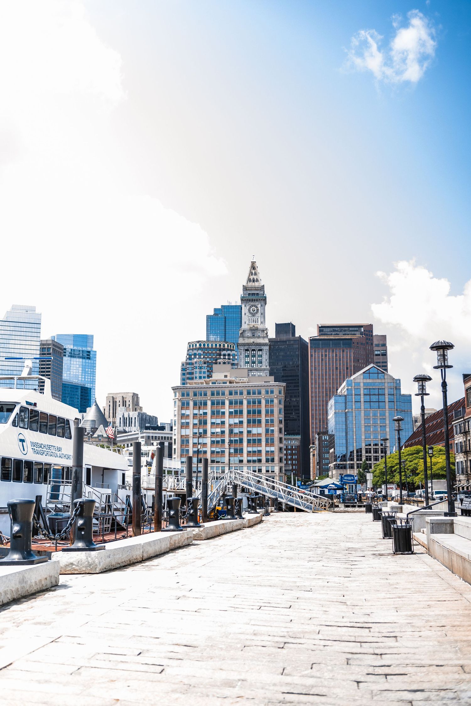 Boston Custom House Tower and downtown skyline viewed from a stone walkway on a sunny day.