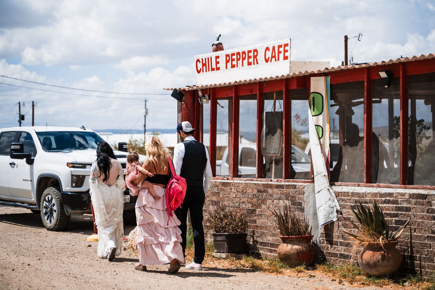 Visitors arriving at the rustic Chile Pepper Cafe with a white SUV parked outside.