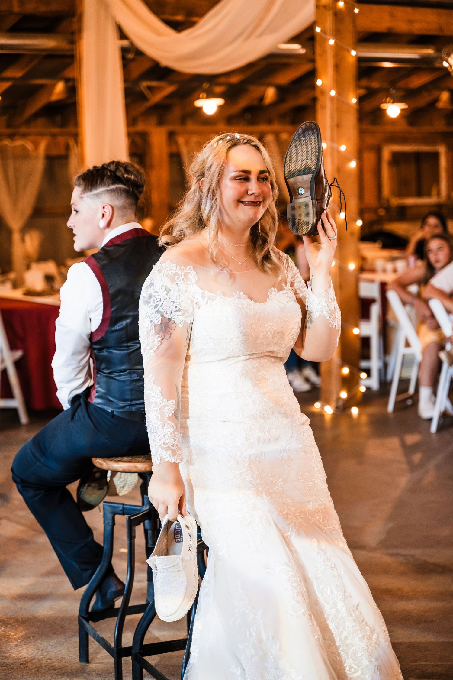 Bride shows off her shoe while sitting at rustic barn wedding reception.