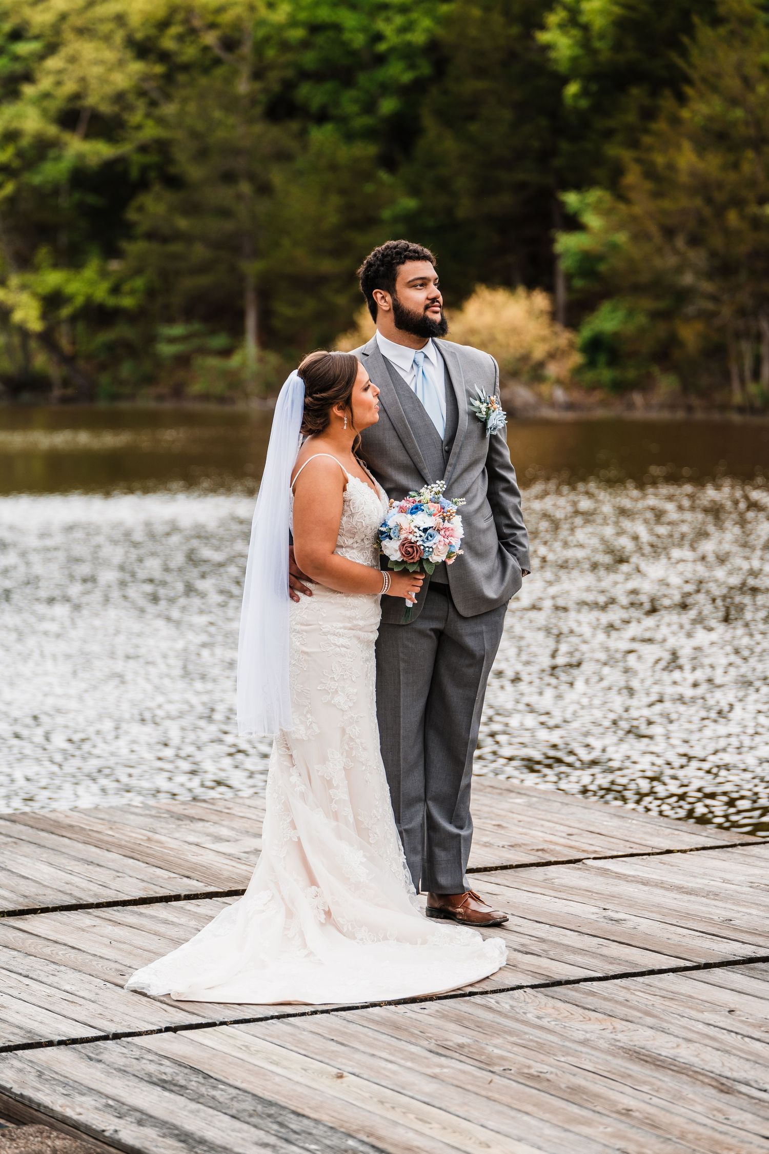 A couple shares an intimate moment on a wooden dock by a lake during their wedding.