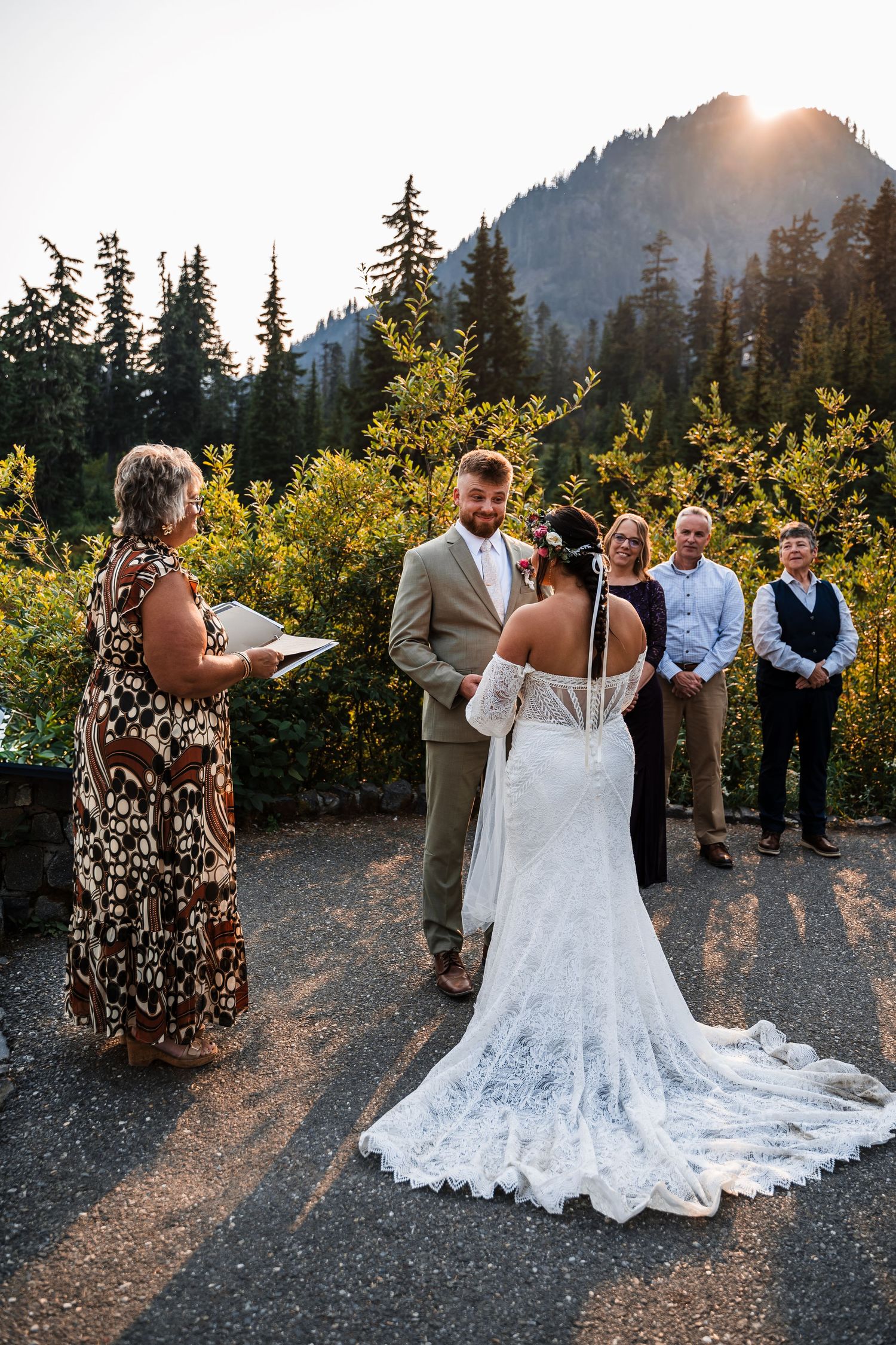 A wedding celebration takes place at sunset with mountain views and guests gathered on a scenic overlook.