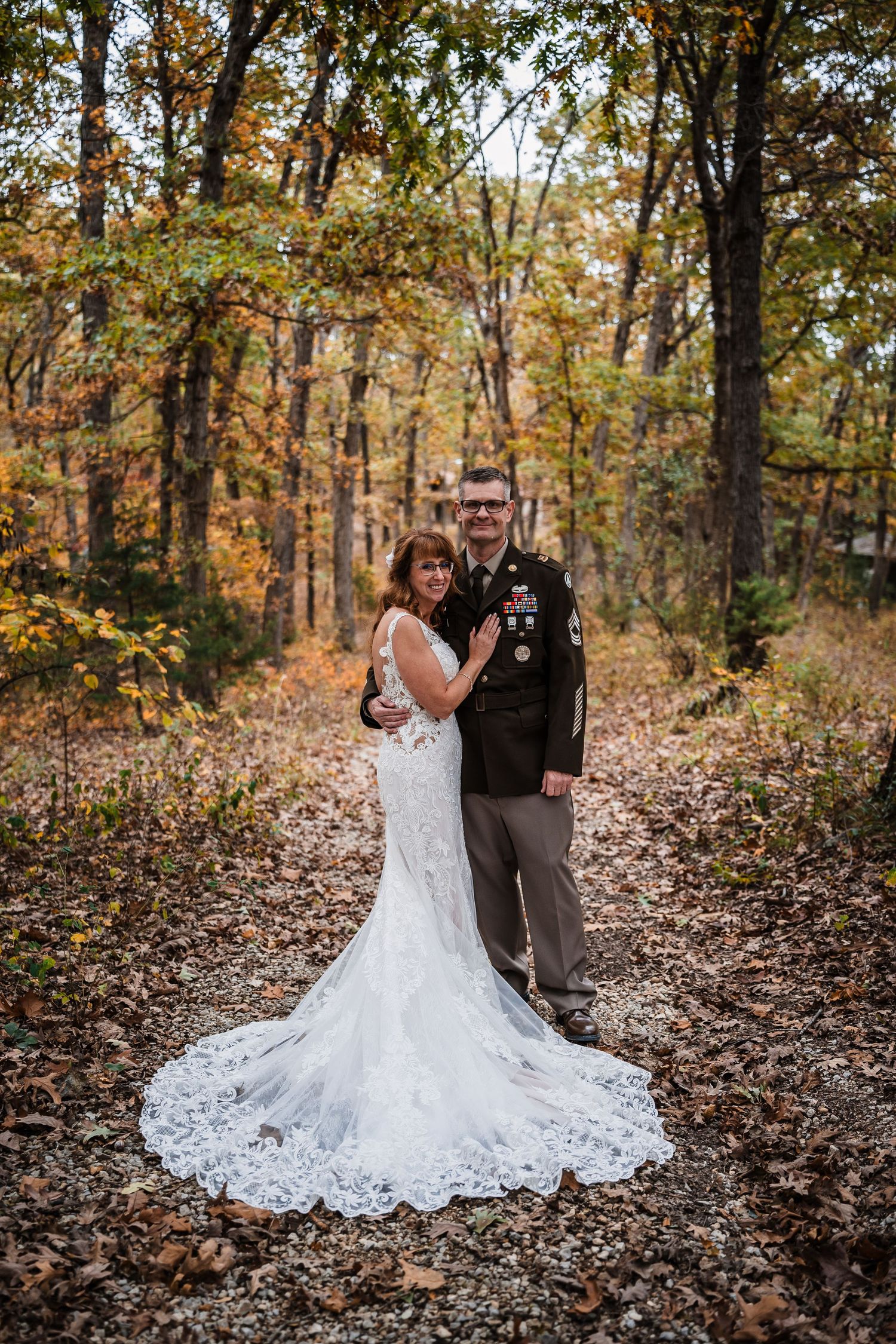 Autumn wedding photos in a forest with fallen leaves and golden trees creating a romantic woodland backdrop.