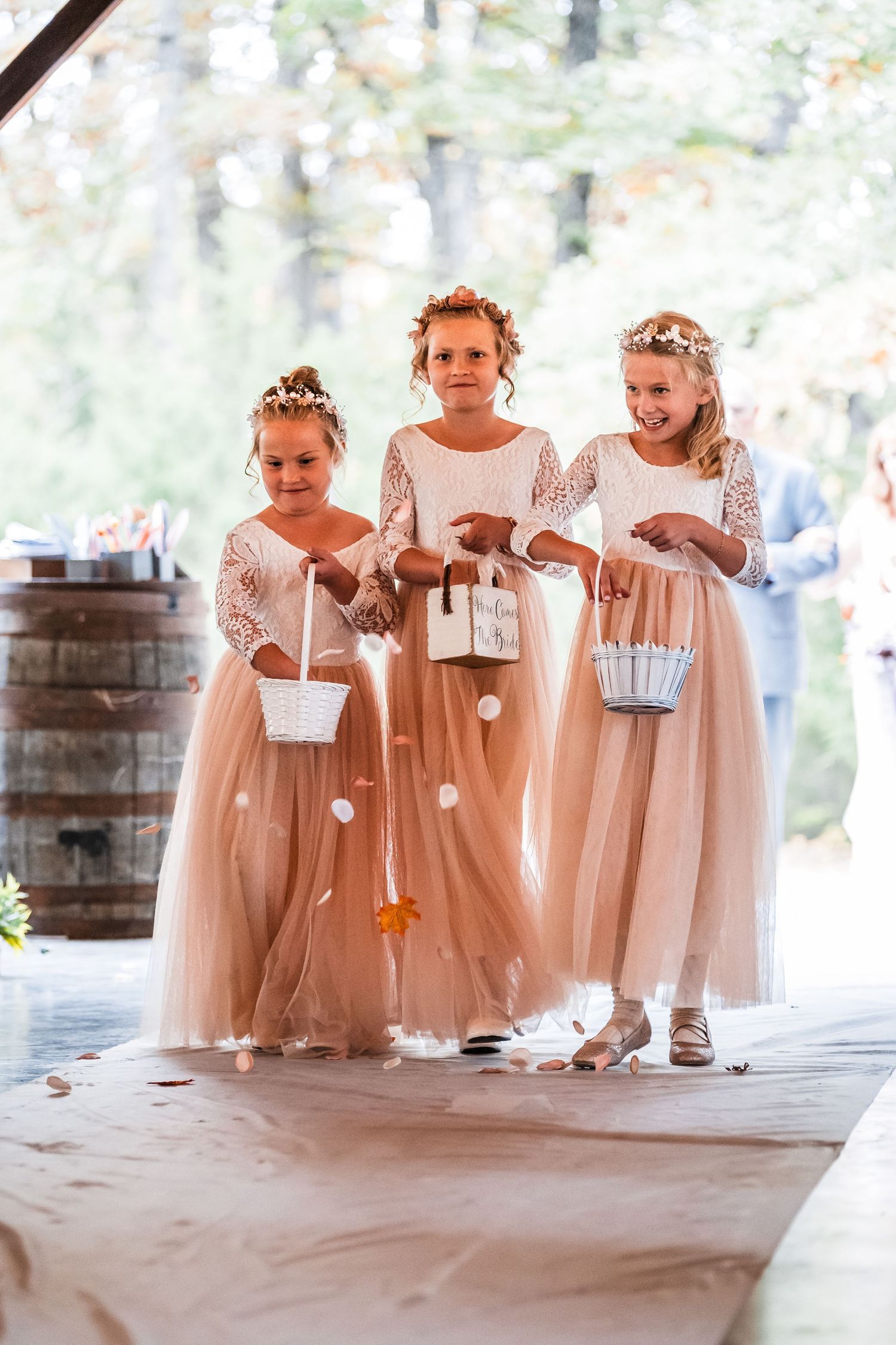 Young flower girls in blush pink dresses with flower crowns standing together at a wedding ceremony.