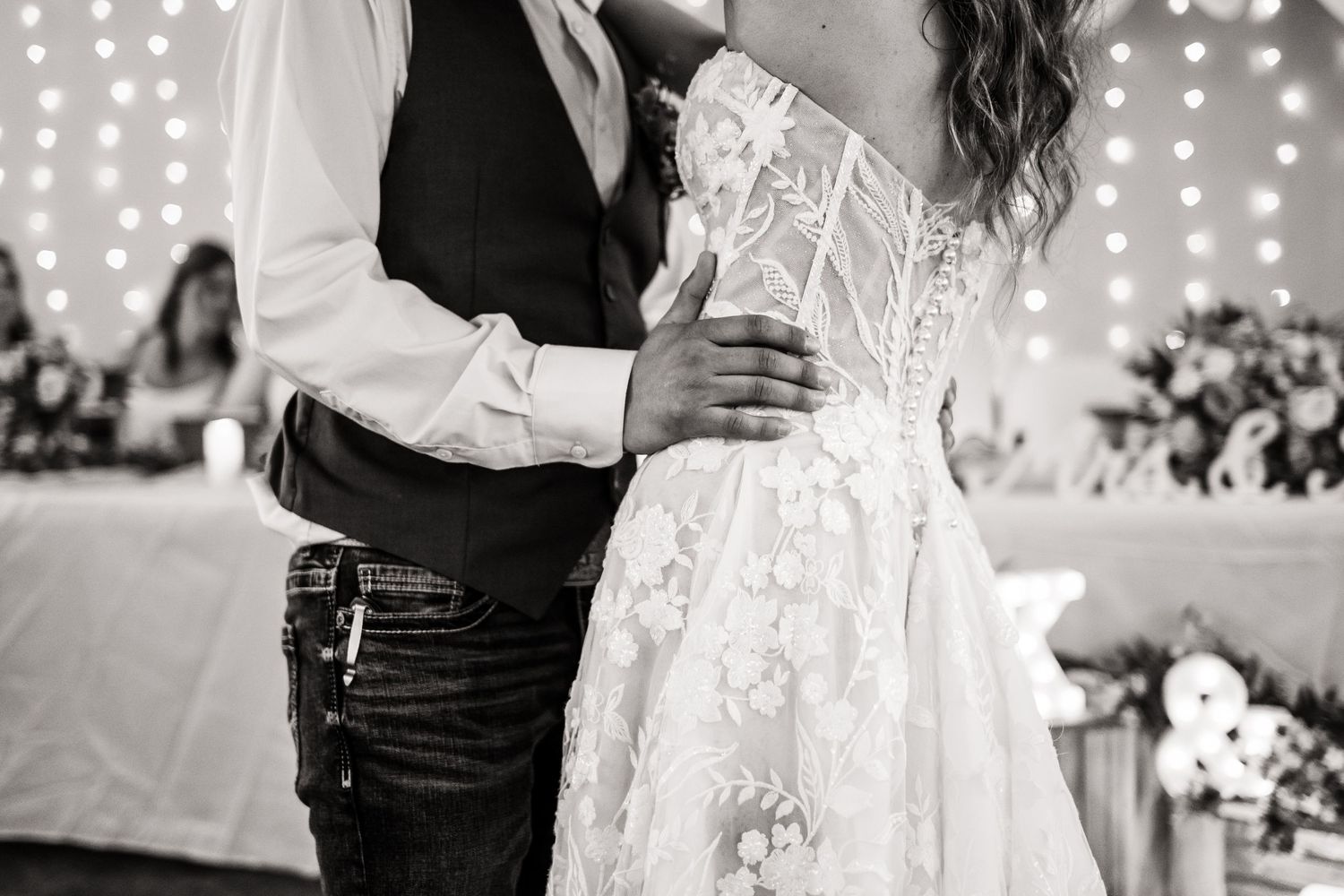 A black and white detail shot of a couple dancing, focusing on the bride's lace wedding dress.
