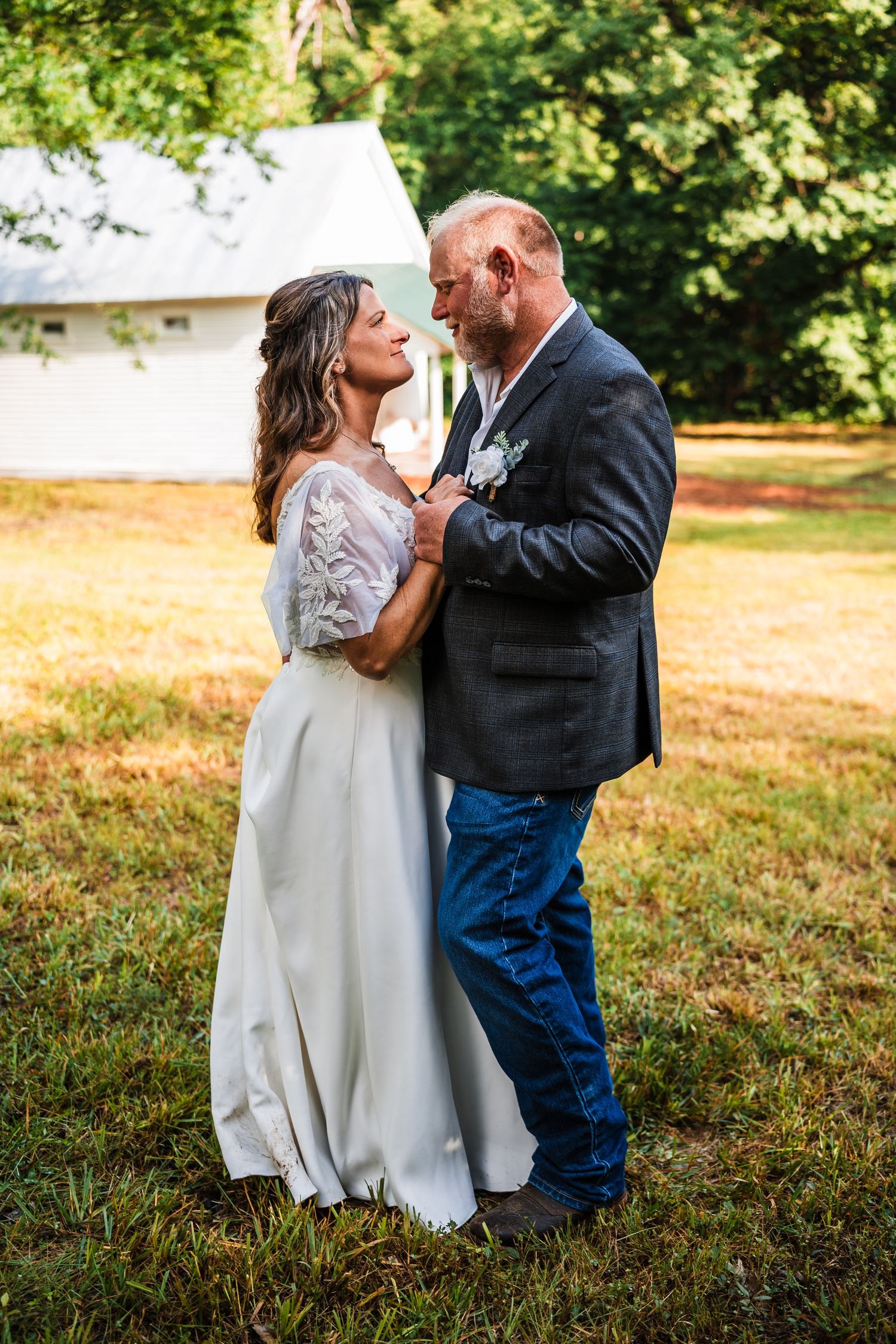 A couple shares an intimate dance together in the grass on a sunny day in a country setting.