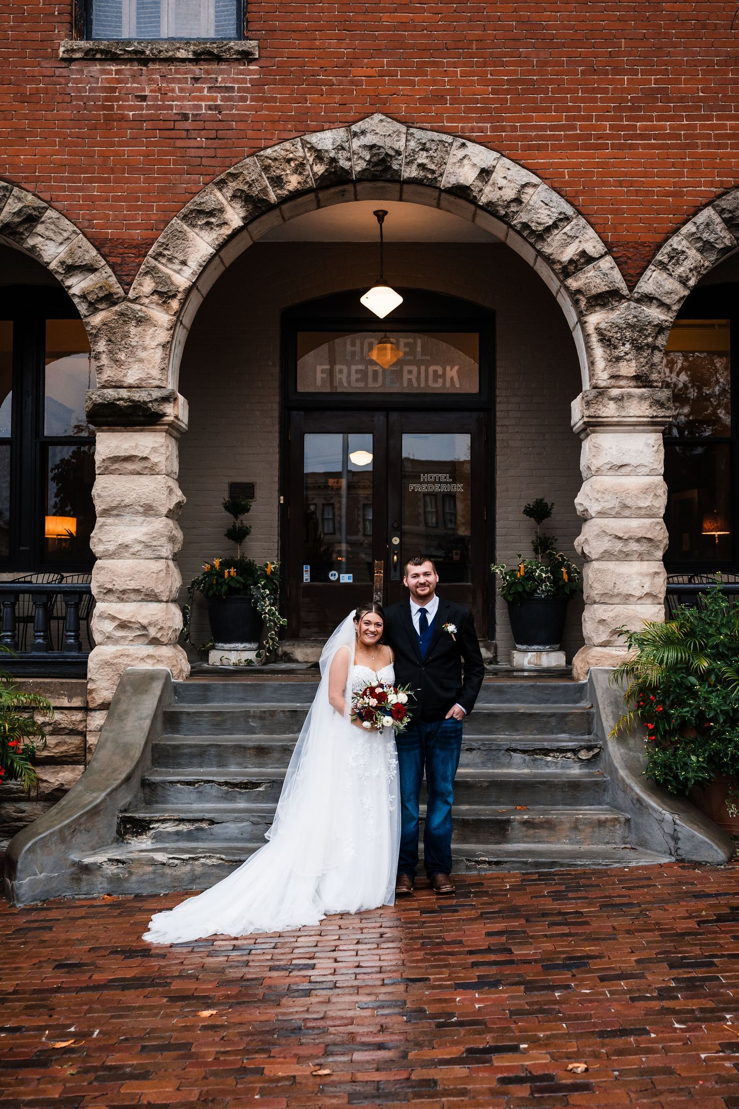 Wedding couple poses under brick archways of historic building with stone columns.