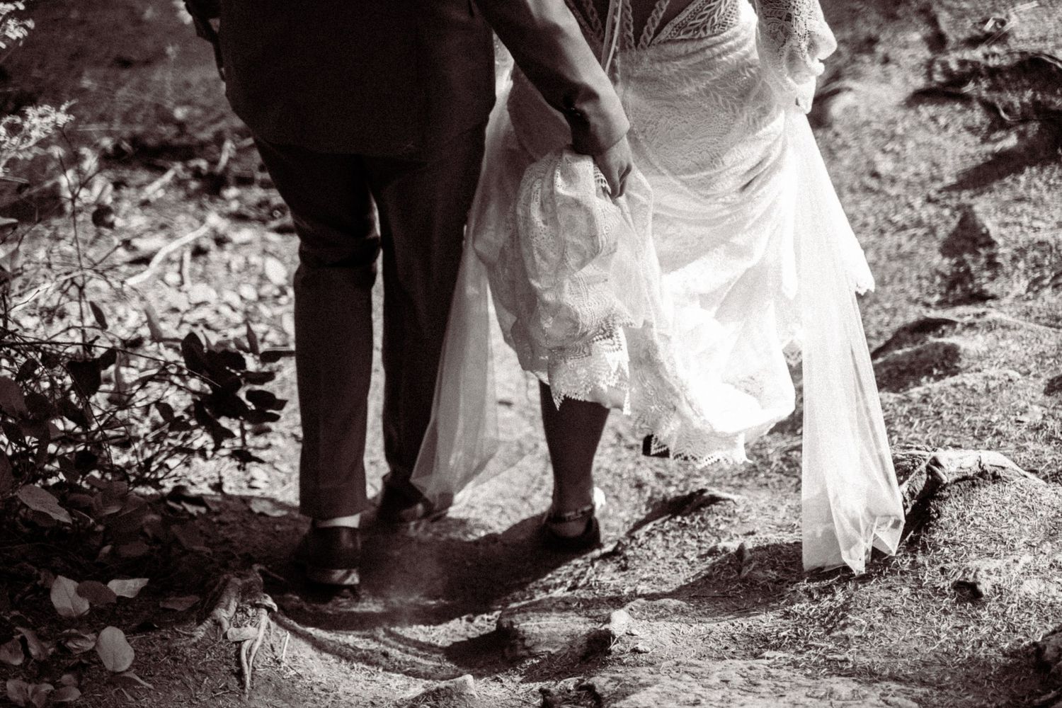 A series of black and white wedding photos showing the bride's dress and shoes as she walks through nature.