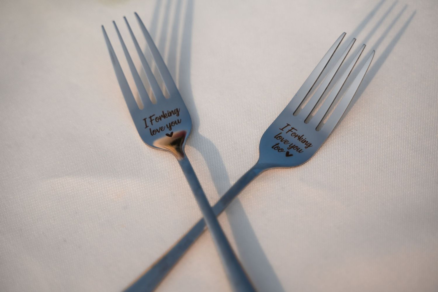 Two silver forks arranged in a crossed pattern on a white surface casting soft shadows.