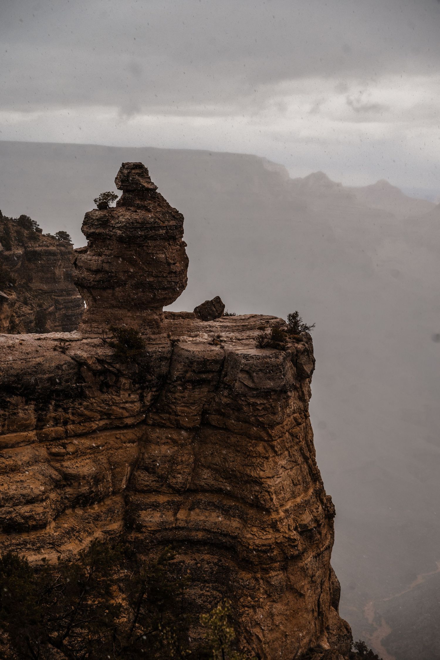 A dramatic rocky cliff formation rises against a misty mountainous backdrop in moody lighting.