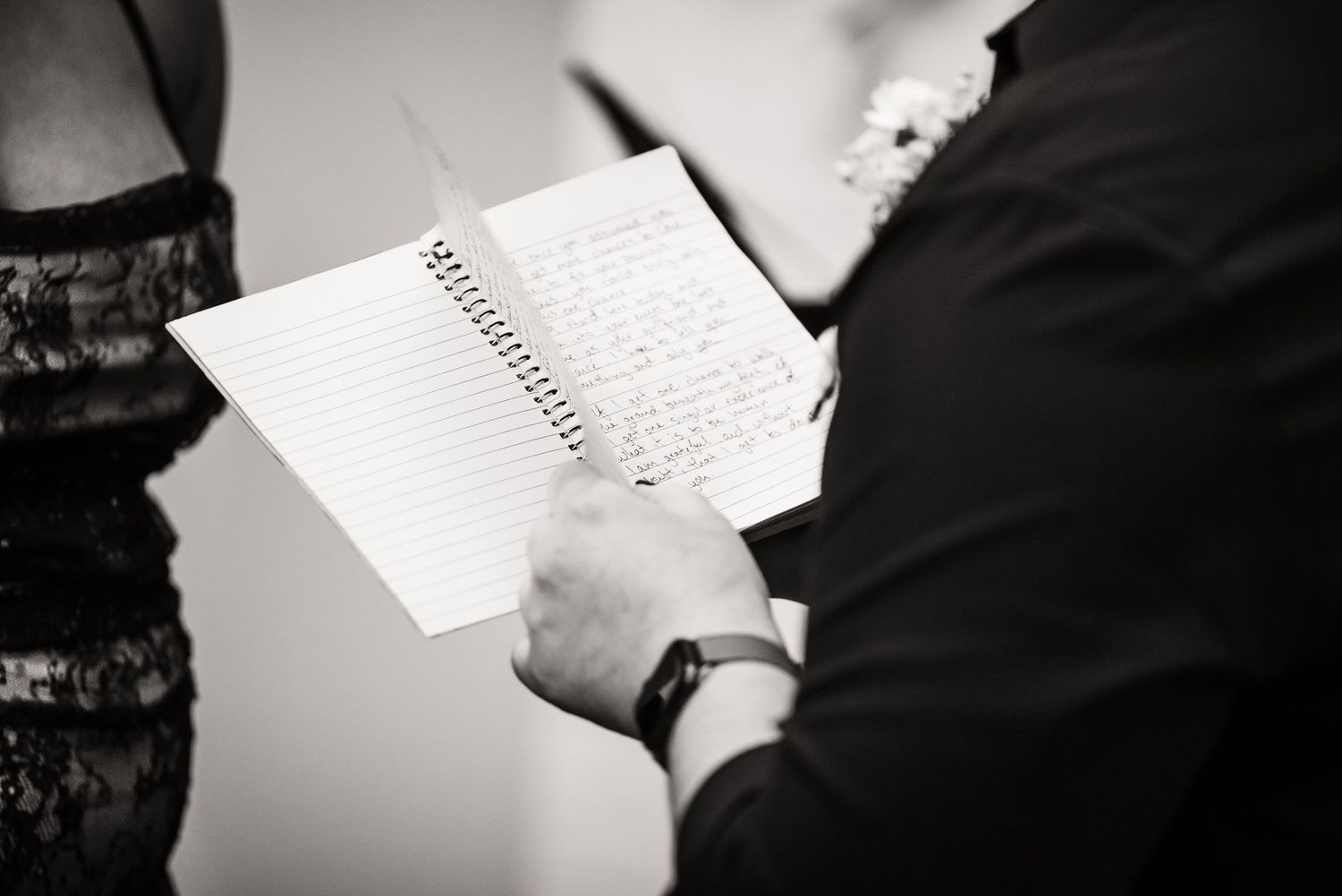 A person holds an open spiral notebook while writing in black and white monochrome photography.
