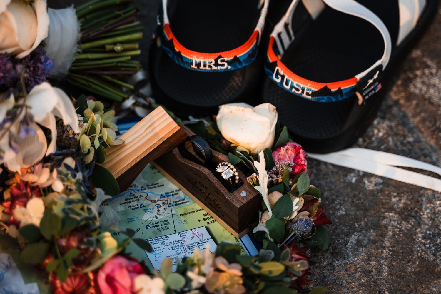 Wedding details including rings and floral arrangements on rustic wooden surface.